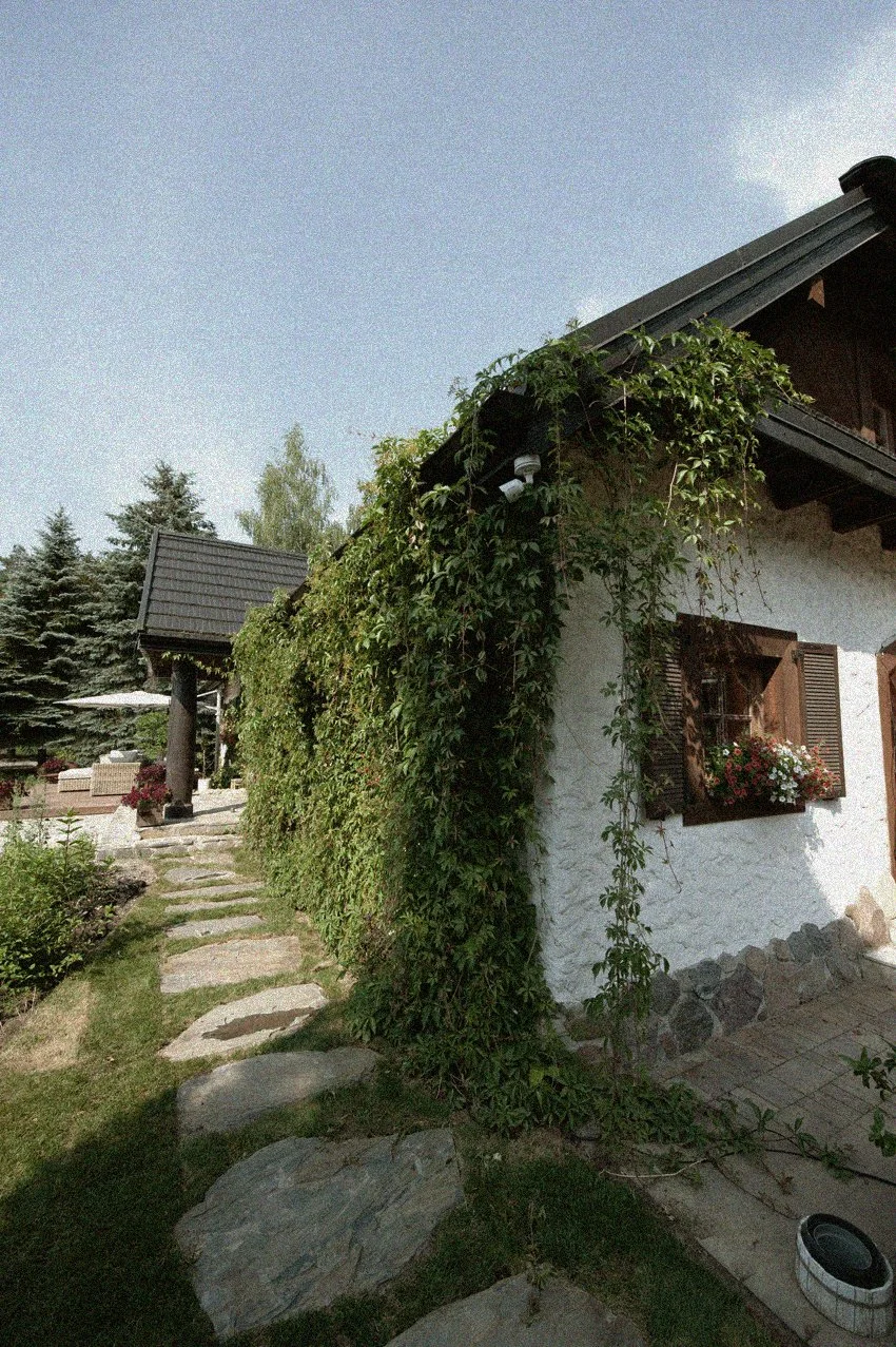 Dom Ananda Retreat House otoczony zielenią, z drewnianymi okiennicami i kamienną ścieżką prowadzącą przez ogród.