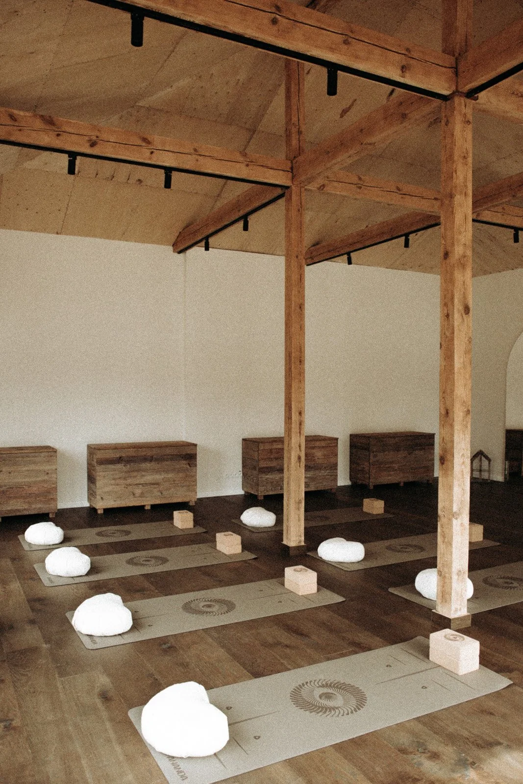 A peaceful yoga or meditation studio with mats, rocks, and blocks arranged on a wooden floor, natural wood beams supporting the ceiling, and minimal decor for relaxation and mindfulness practice.