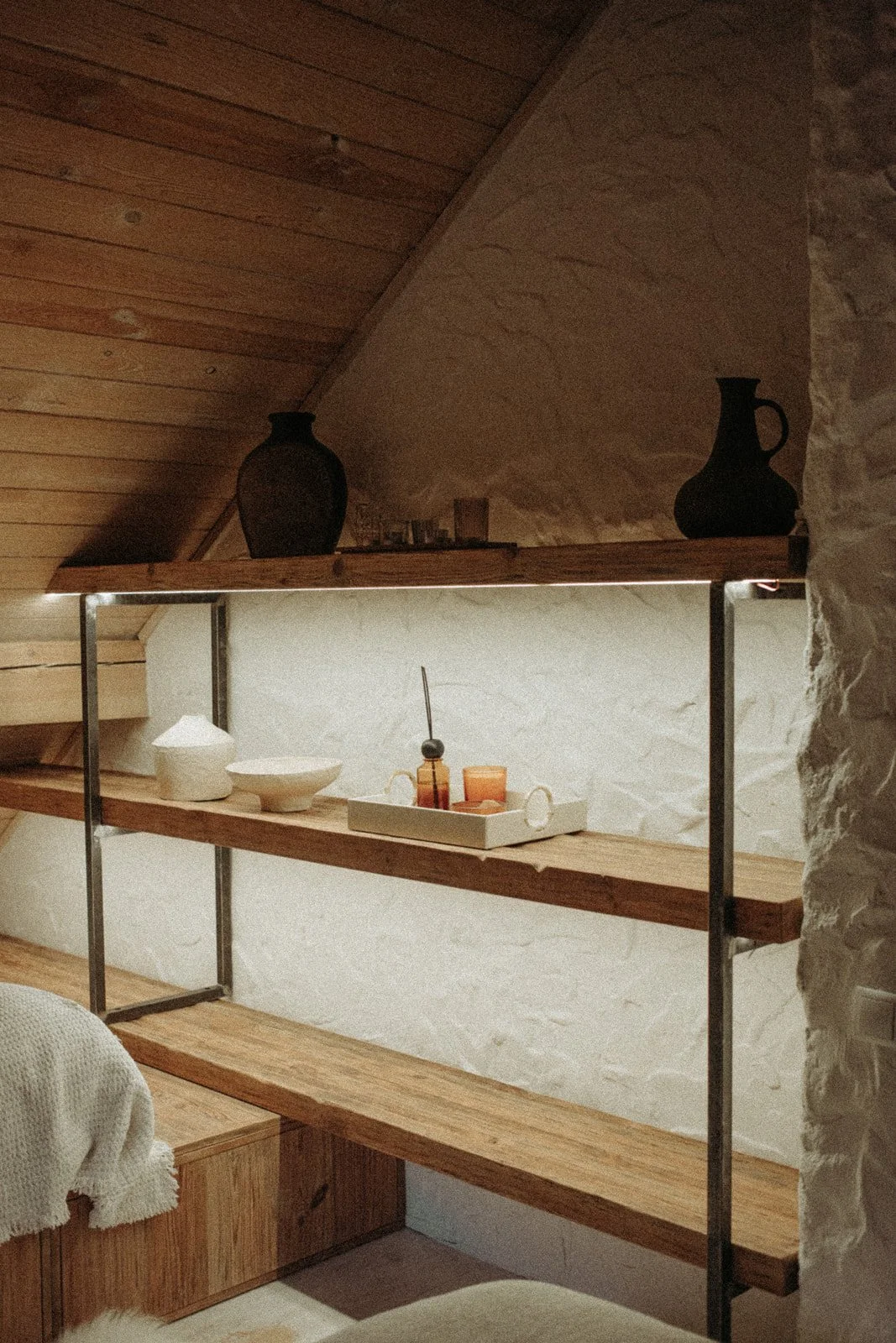 Wooden shelves with decorative vases, bowls, and candles against a textured white wall in a cozy interior.