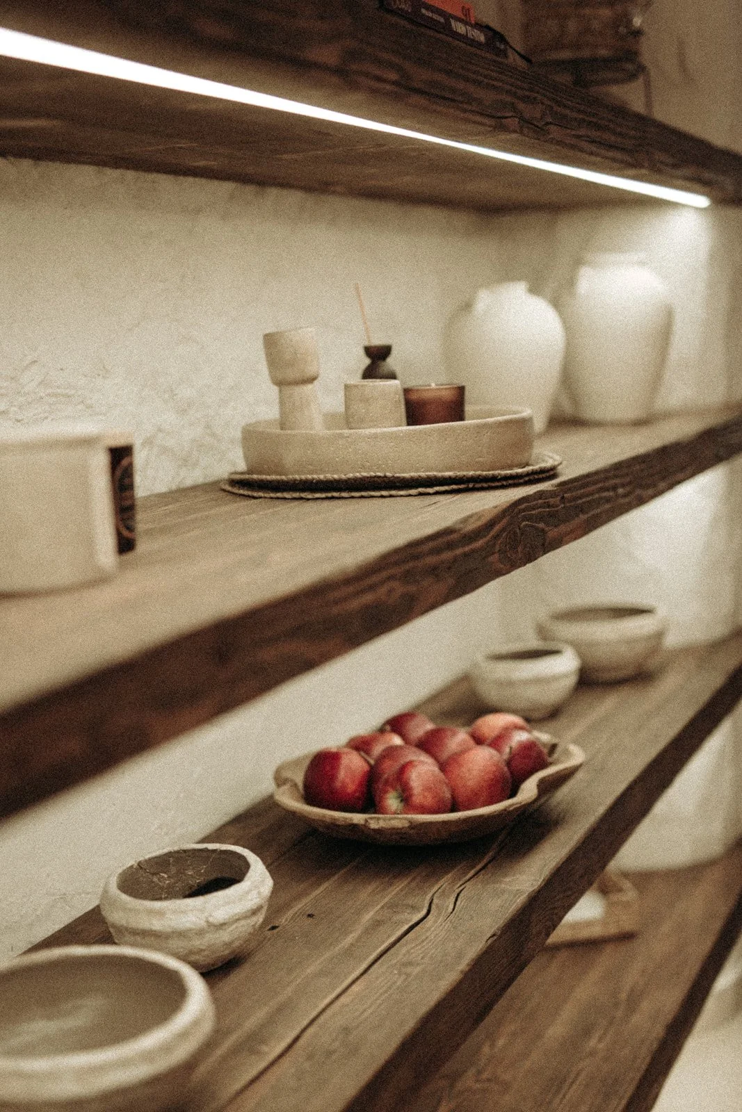 Drewniane półki z ceramiką, dekoracjami i świeżymi jabłkami we wnętrzu Ananda Retreat House.