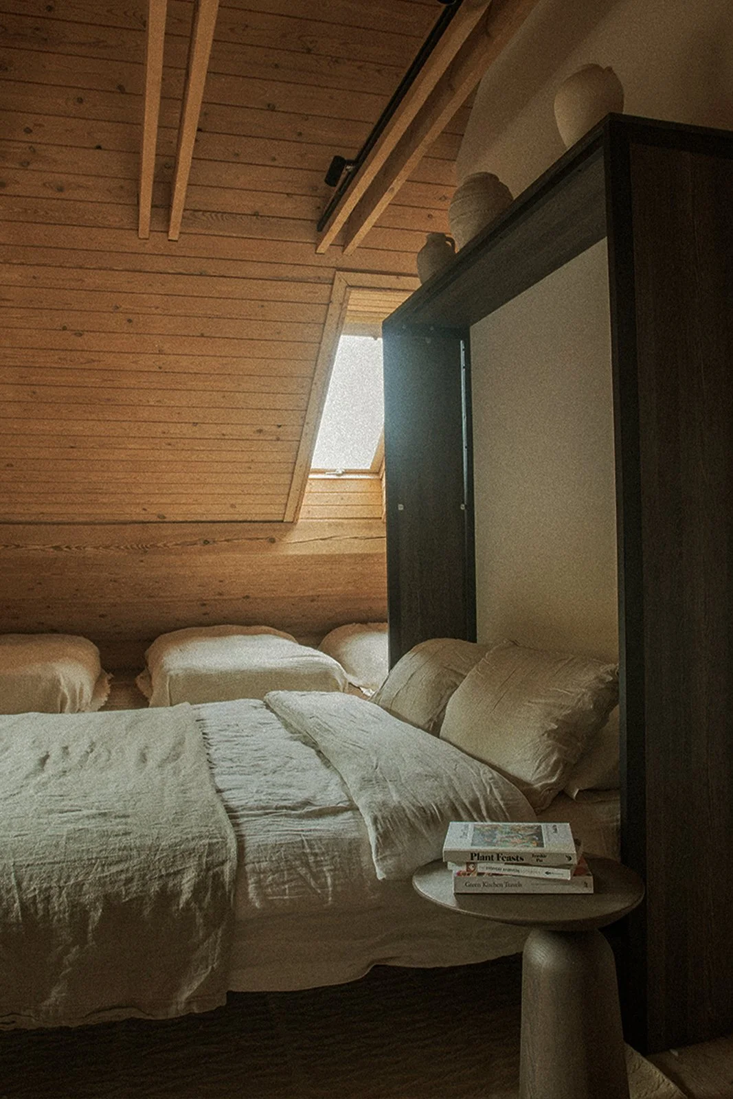 Sypialnia na poddaszu w Ananda Retreat House z drewnianym wnętrzem, naturalnymi materiałami i oknem dachowym.