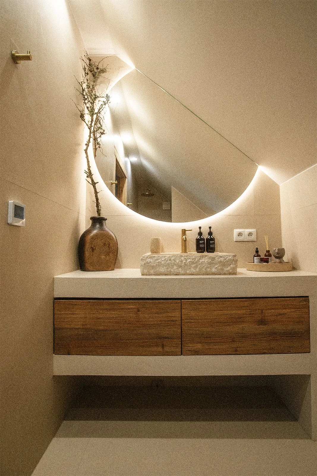 Minimalistyczna łazienka w Ananda Retreat House z kamienną umywalką, okrągłym lustrem i naturalnymi dekoracjami.