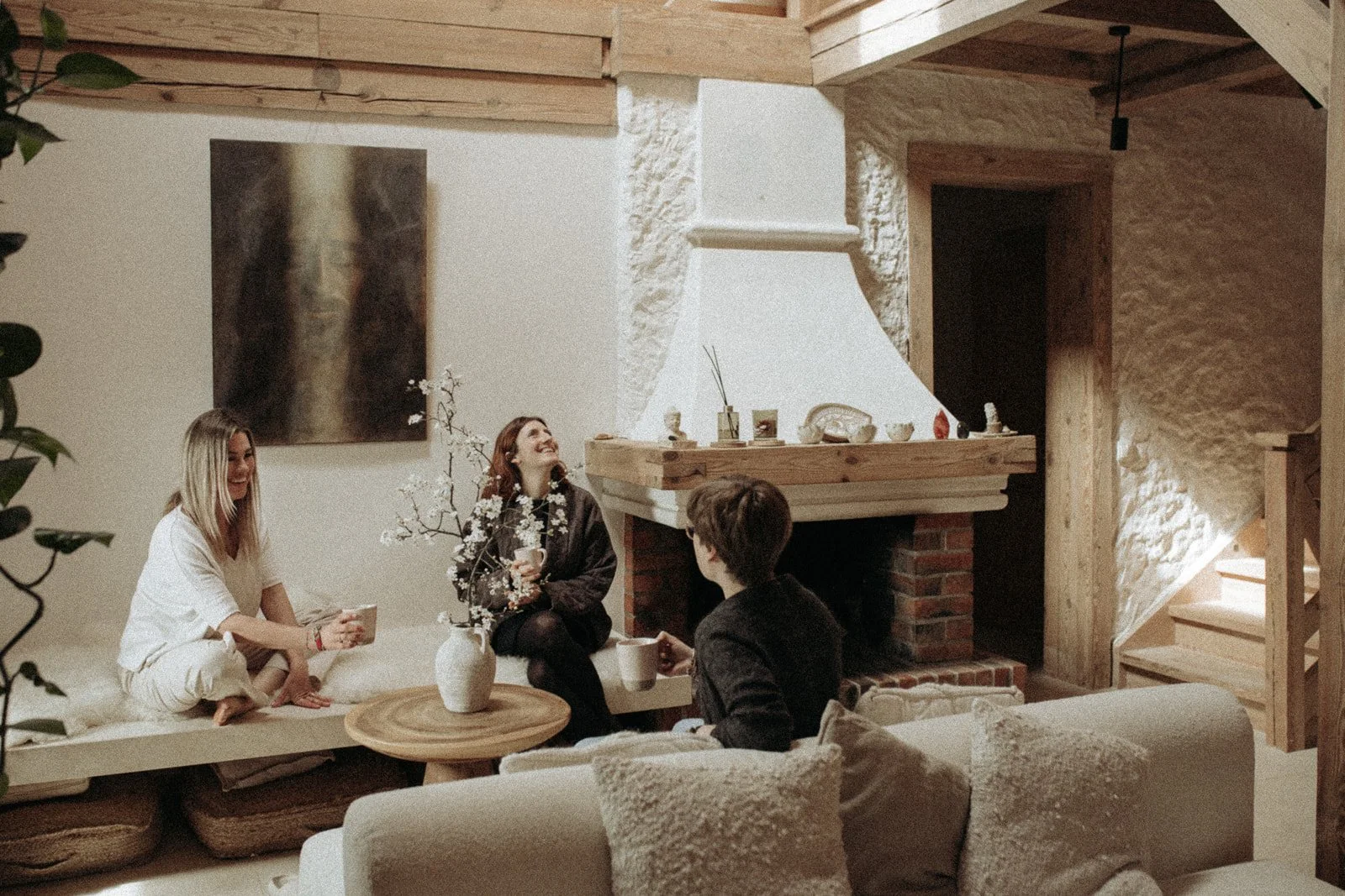 Trzy osoby spędzające wspólnie czas w salonie Ananda Retreat House, rozmawiające i odpoczywające przy kominku.