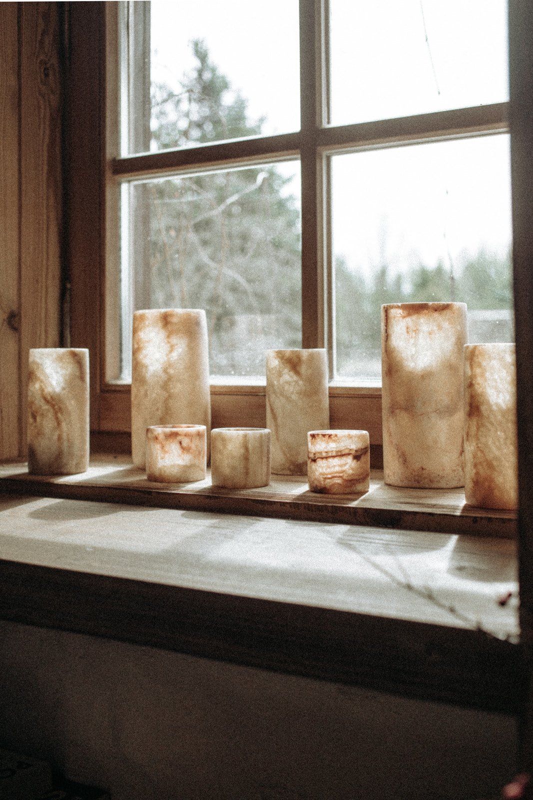 Collection of salt lamps on window sill with wooden wall and window in the background