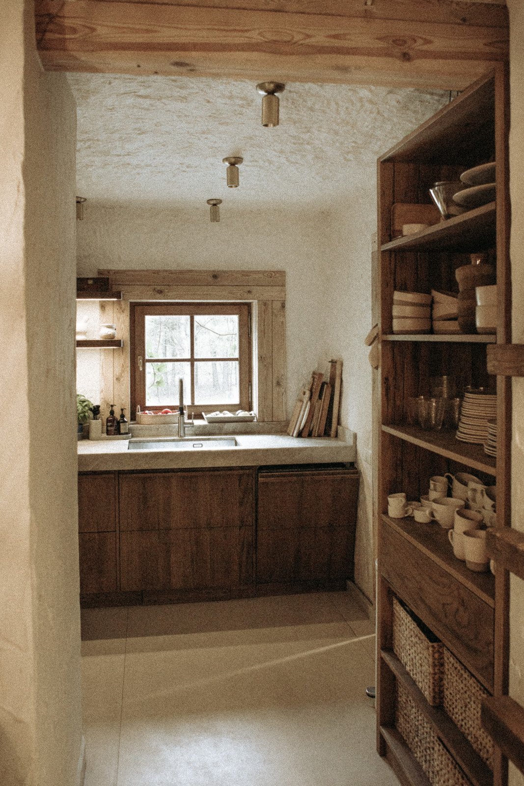 Kuchnia w Ananda Retreat House z drewnianą zabudową, otwartymi półkami i naturalnym wystrojem.