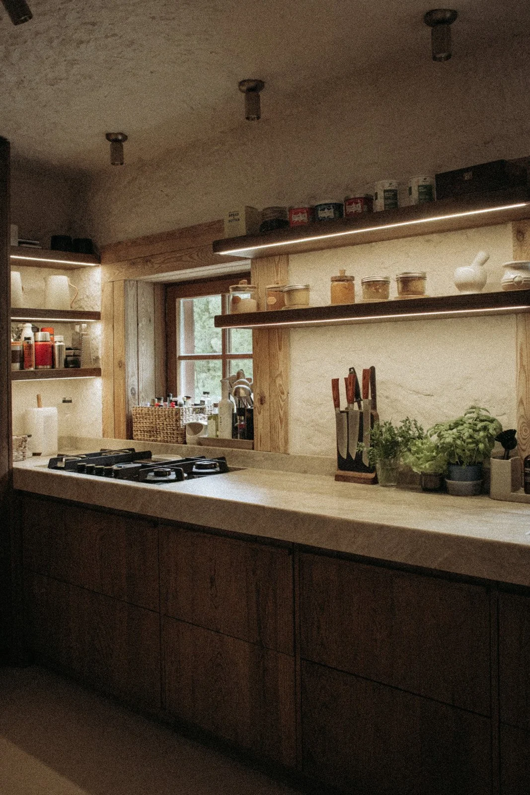 Kuchnia w Ananda Retreat House z drewnianą zabudową, otwartymi półkami i naturalnymi dodatkami.