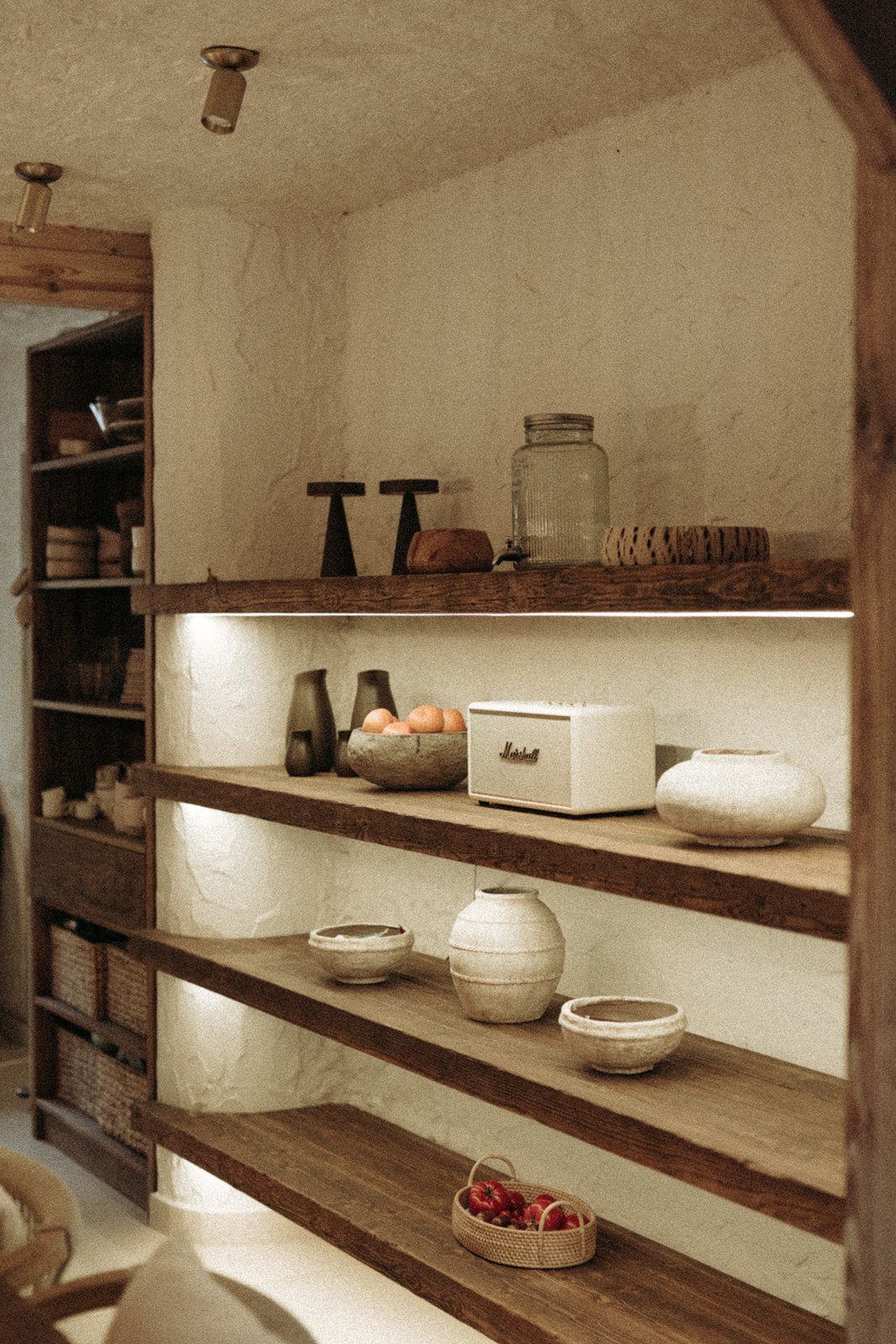 Drewniane półki z ceramiką, dekoracjami i jabłkami we wnętrzu Ananda Retreat House.