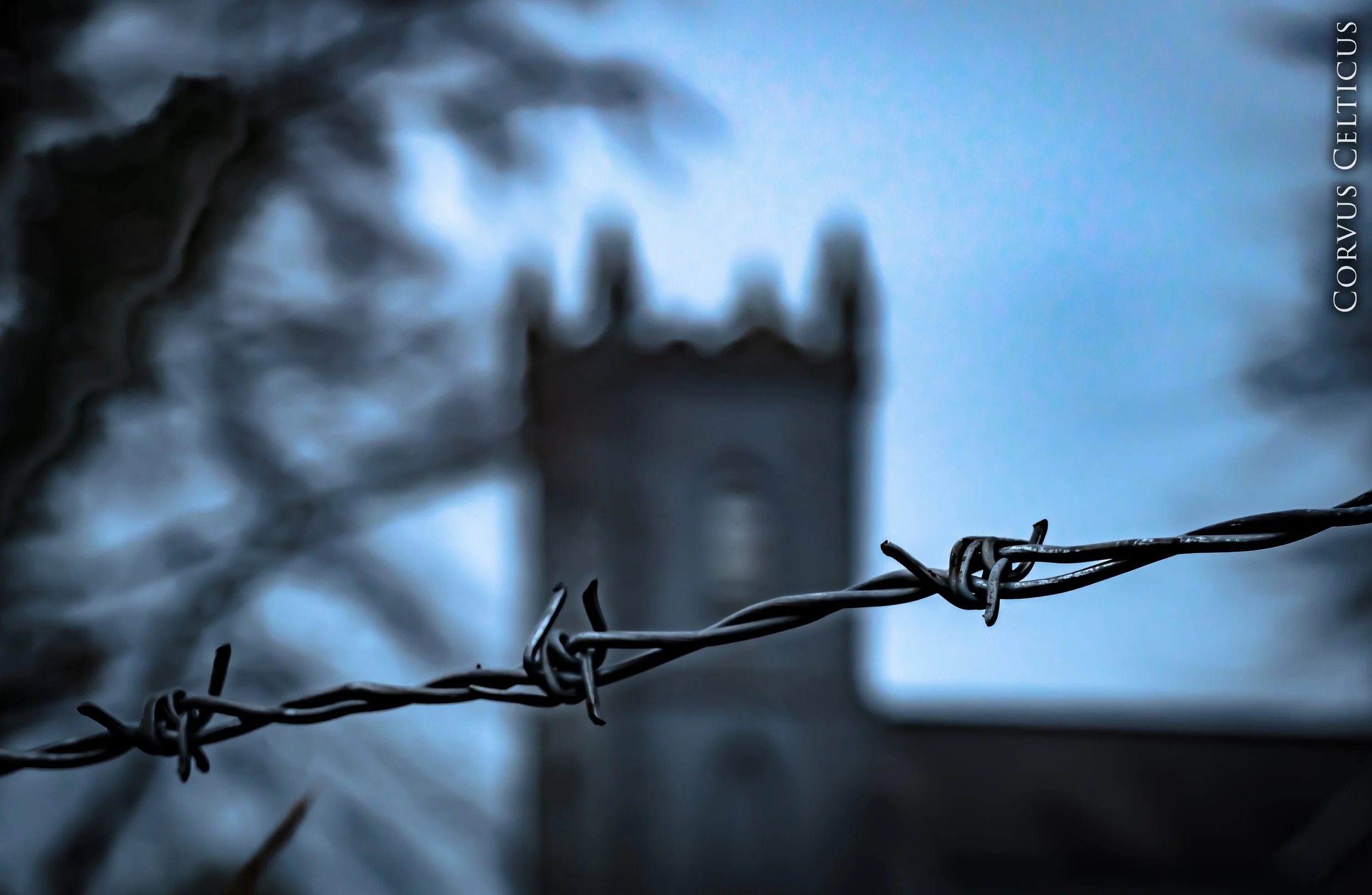 Close-up of a barbed wire fence with Castledawson Prebyterian church blurred in the background - a cloudy sky.