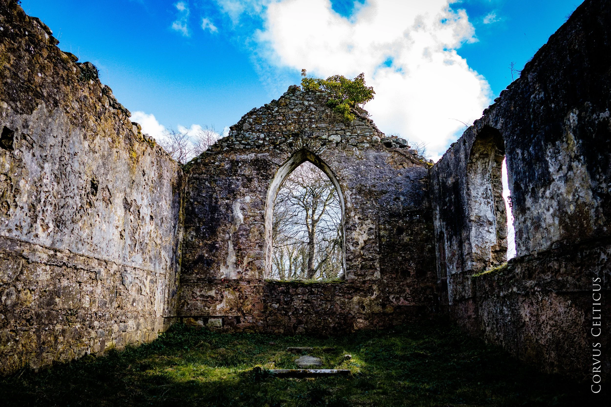 Ancient stone ruins of Kilcronaghan old church, against a bright blue sky with clouds.