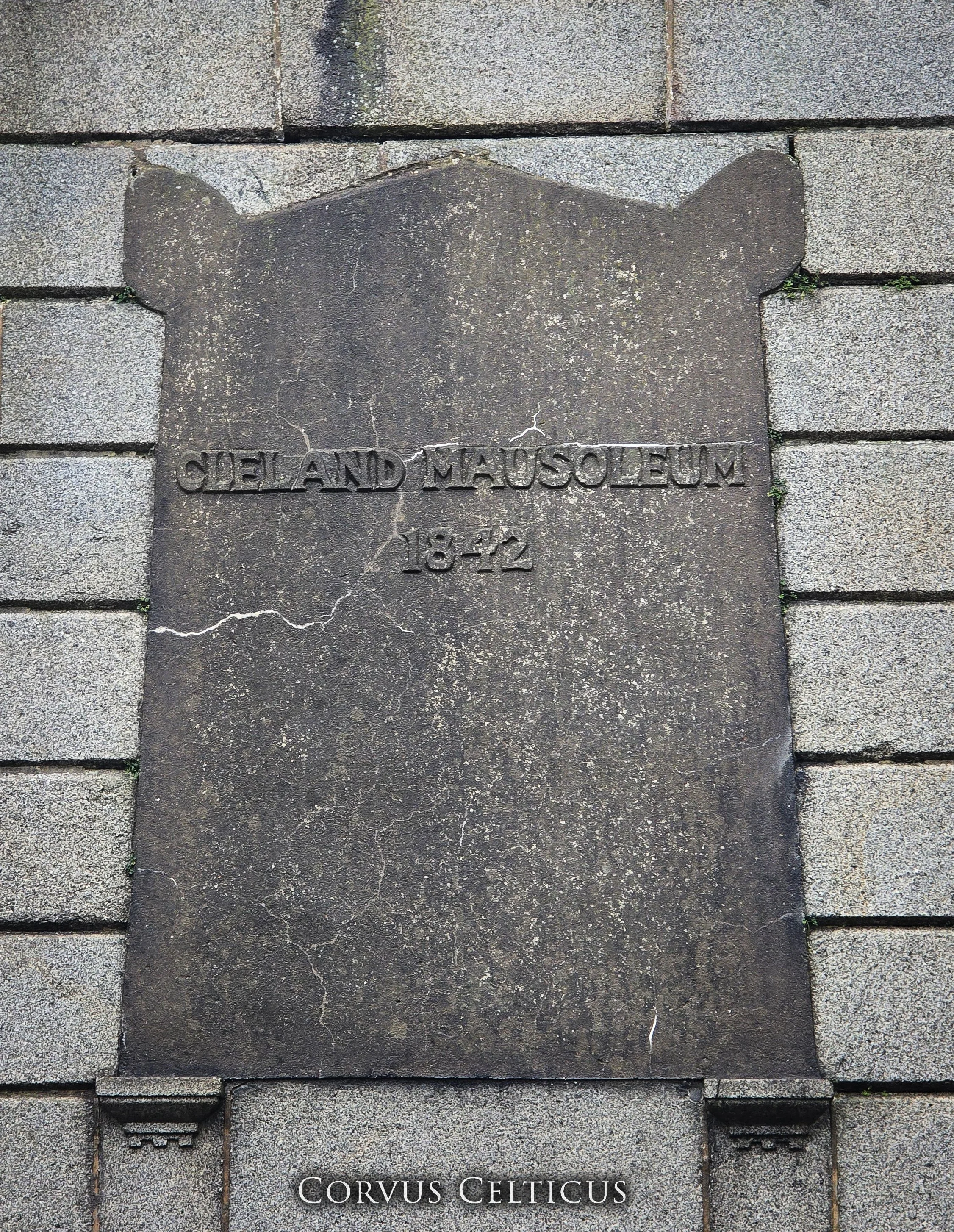 Stone plaque embedded in a brick wall, with the inscription 'CLELAND MAUSOLEUM 1842'