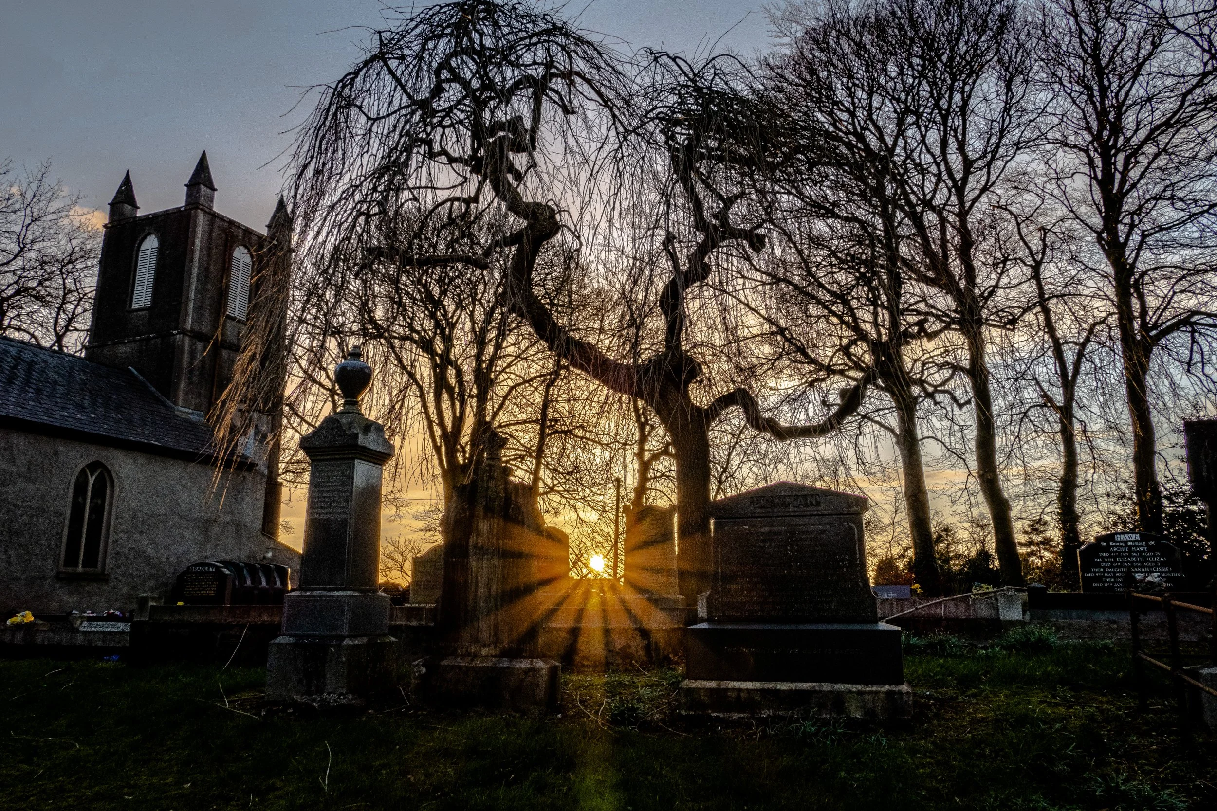 Knockloughrim sunset: Sunset behind leafless trees and a graveyard, with a church building visible on the left.