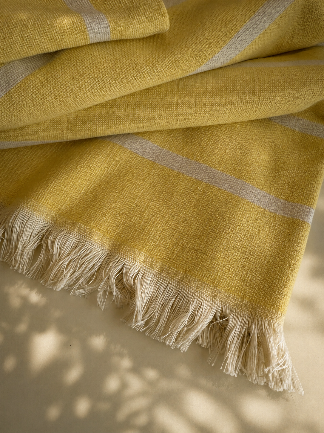 Close-up of a yellow woven beachtowel with white stripes and fringed edge.