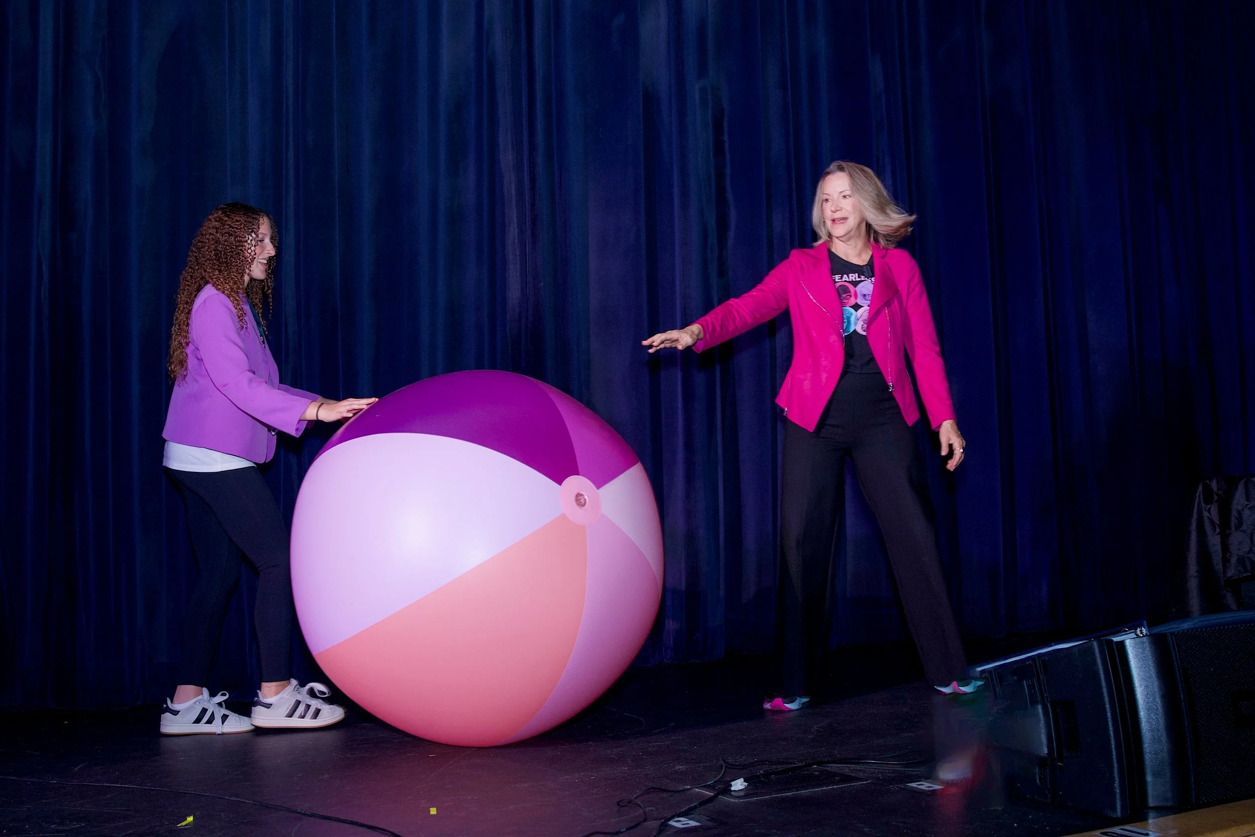 Ellen Claire and a volunteer audience member on stage exploring aspects of the Empower the Girls program through the physical metaphor of a beach ball.