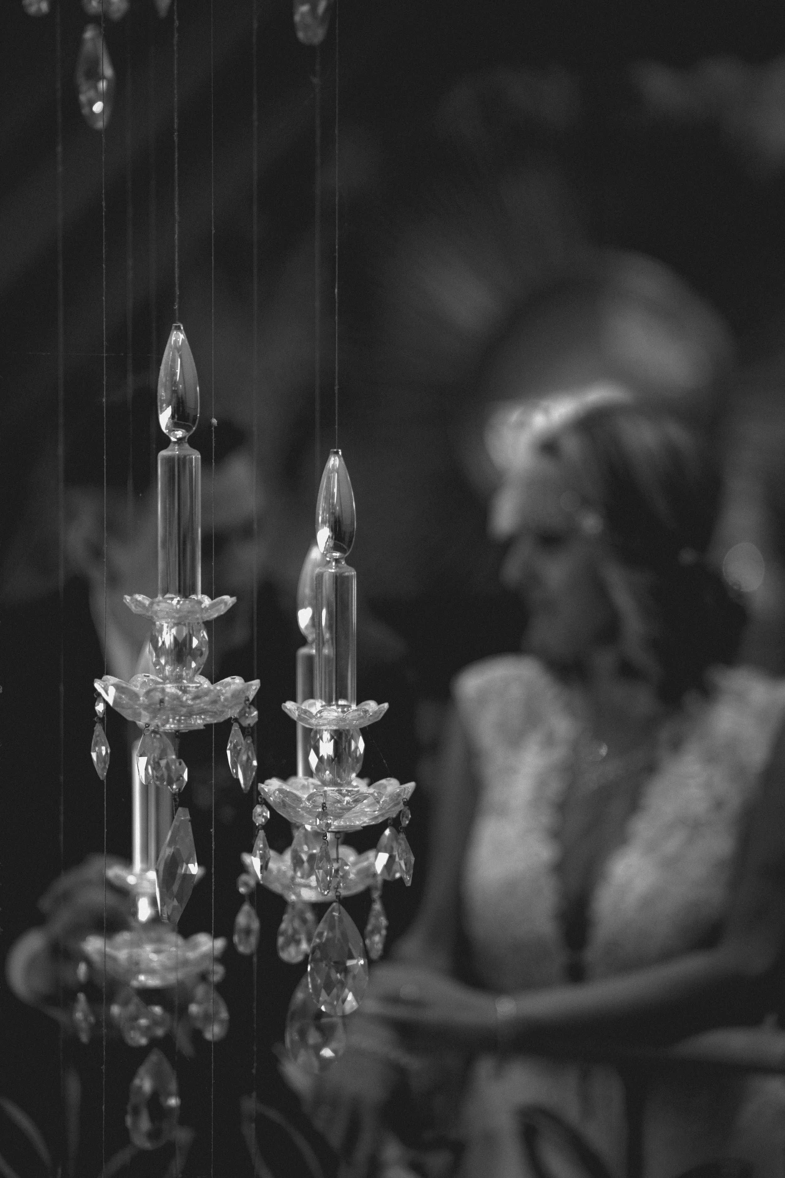 Close-up of a crystal chandelier with multiple hanging glass or crystal ornaments, with a blurred figure in the background.