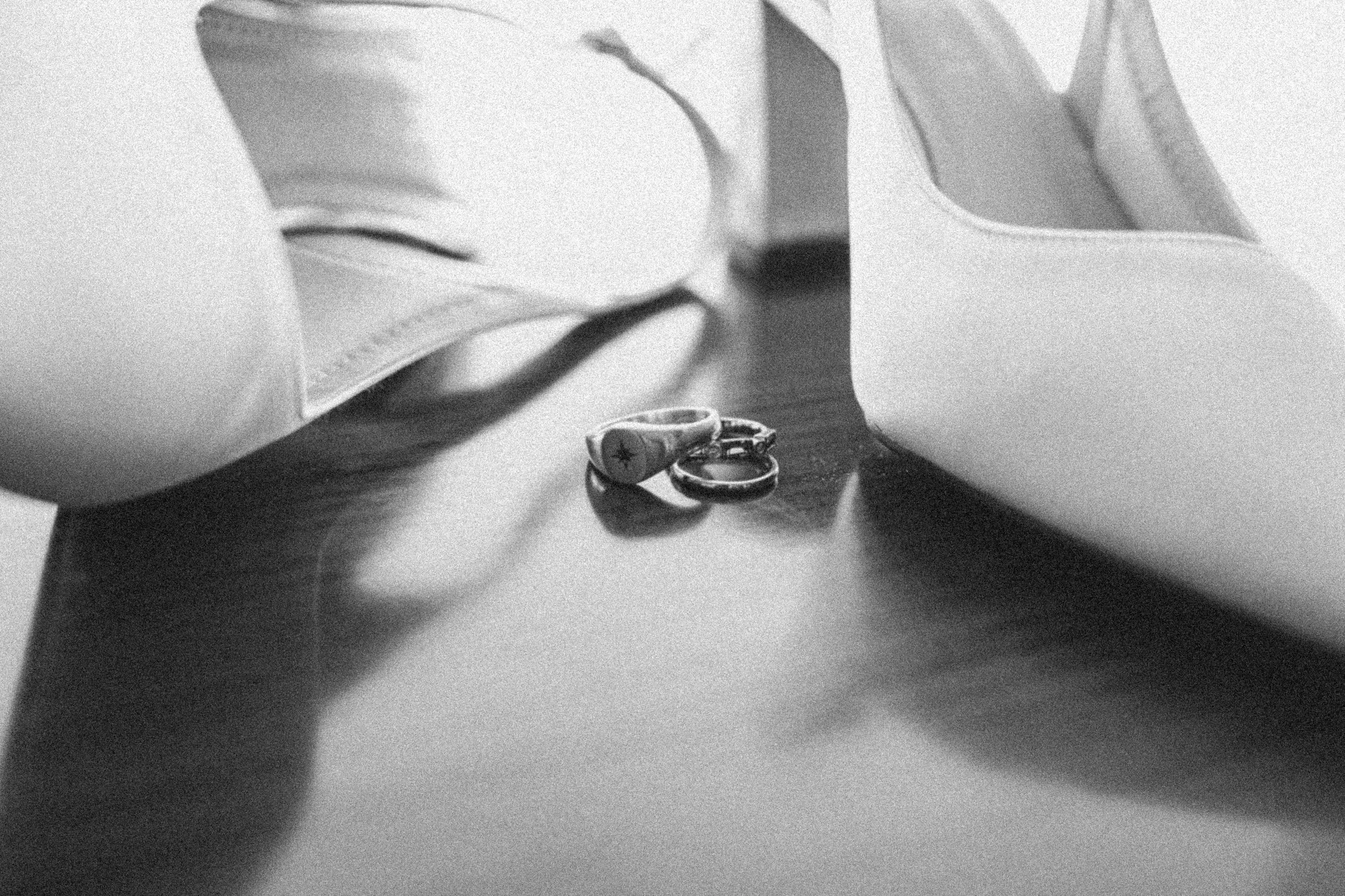 Black and white photograph of a small pile of rings, including wedding bands, placed on a surface between two books