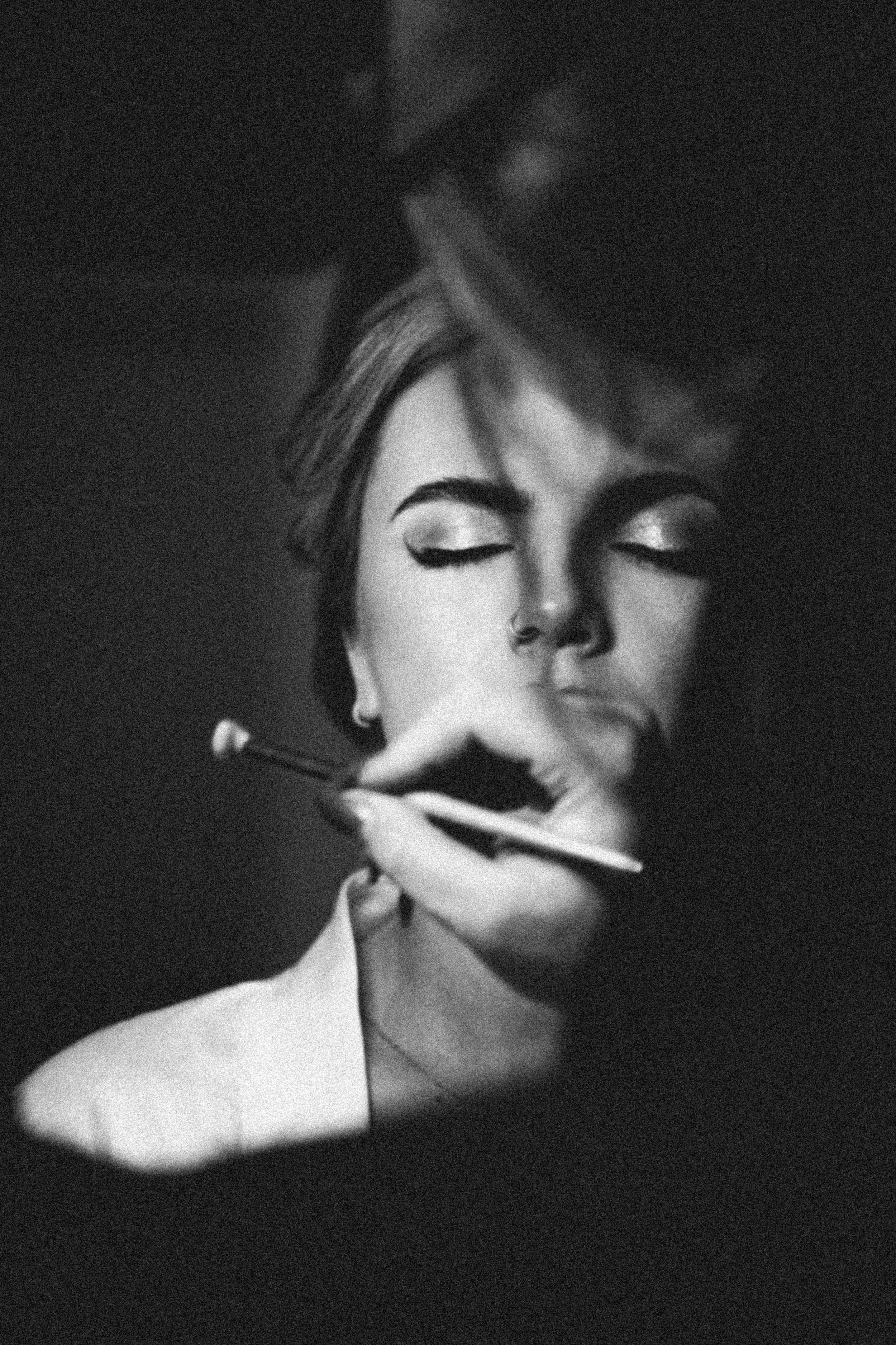 Black and white photo of a woman with eyes closed, holding a makeup brush near her face, with her head slightly tilted.