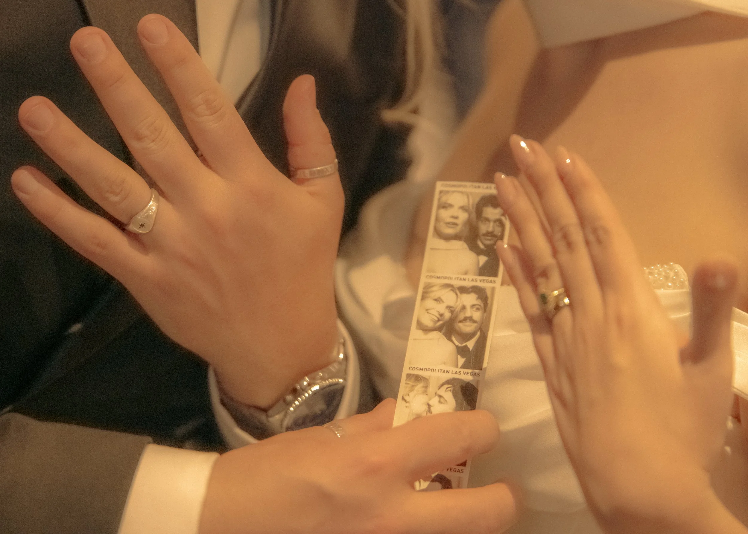 Close-up of people’s hands holding vintage black-and-white printed paper photo booth strips, featuring images of a man and woman, in an indoor setting with warm lighting.