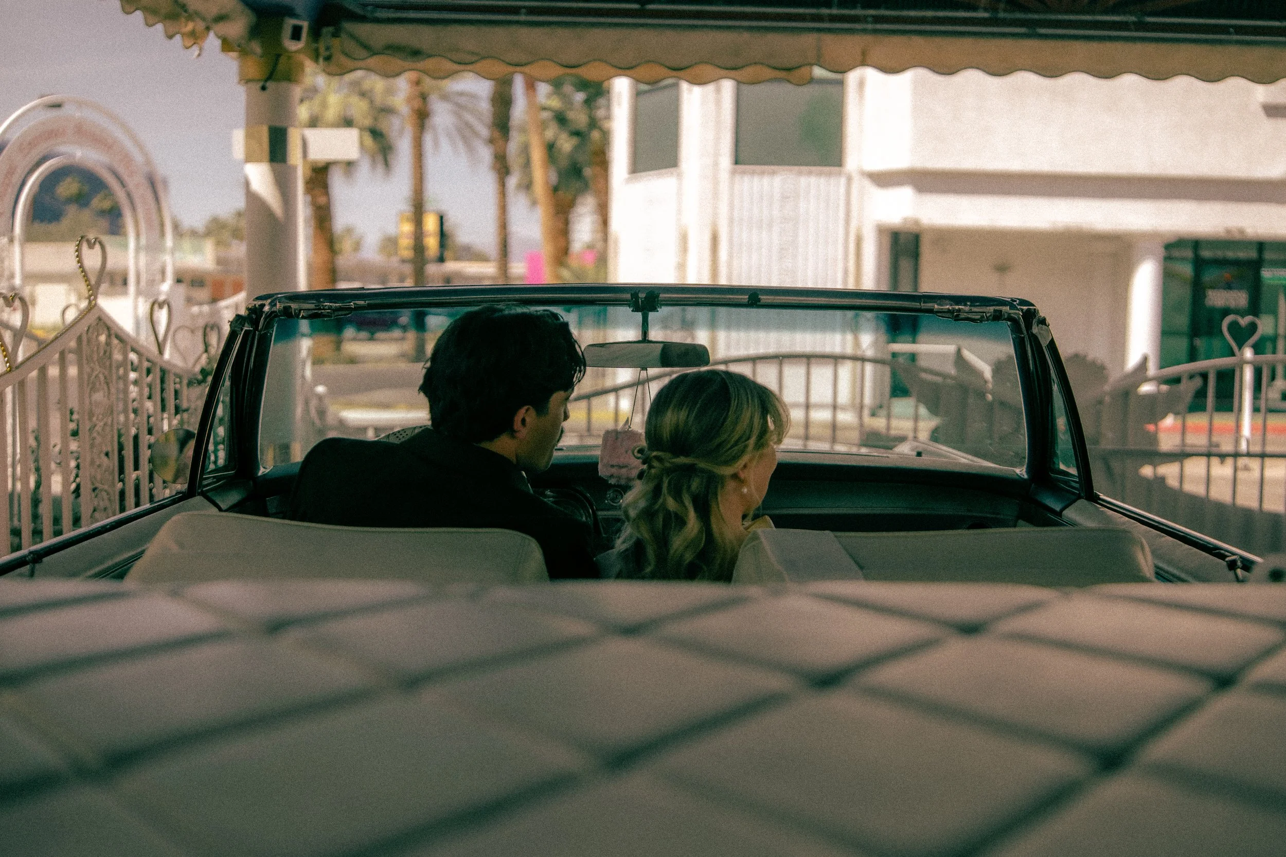 A car with two people inside, sitting in the front seats, with a view of a suburban street outside.