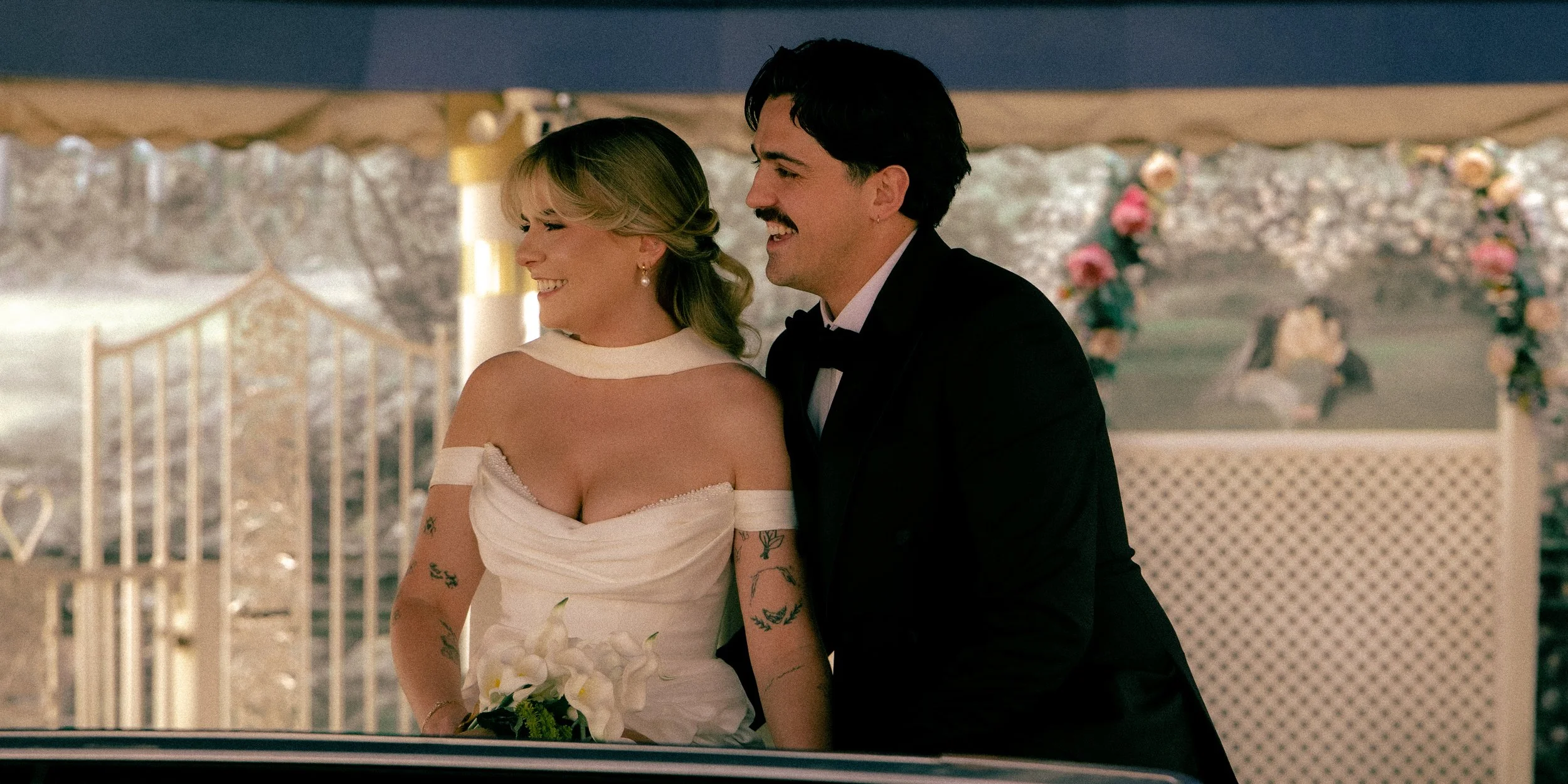 A bride and groom sharing a joyful moment at their wedding reception, with the bride holding a bouquet of flowers and both dressed in formal attire.