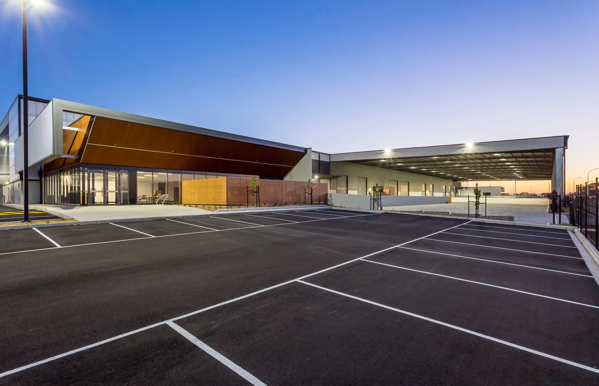 Empty parking lot in front of a modern building during twilight with a clear sky.