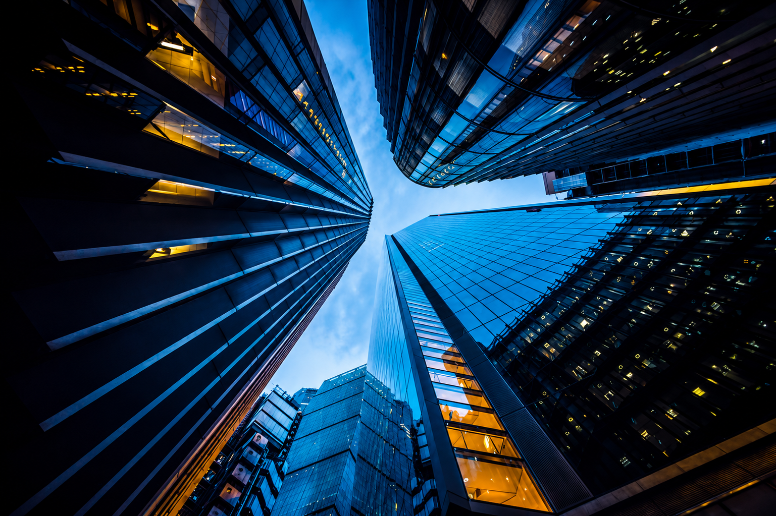 Looking up at modern glass skyscrapers in a city with a blue sky in the background.