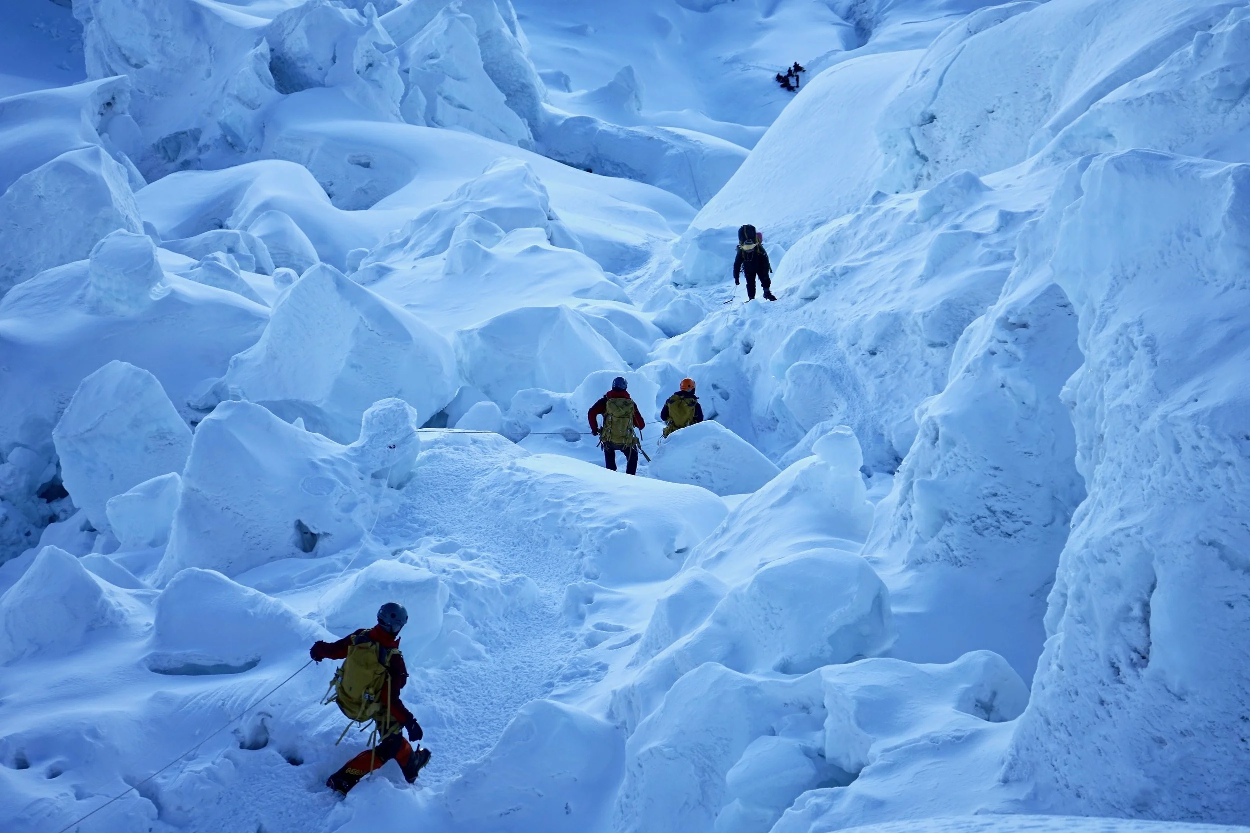 A group of mountaineers climbing a snow-covered icy slope in a glacier. They are wearing winter gear and carrying backpacks and other climbing equipment.