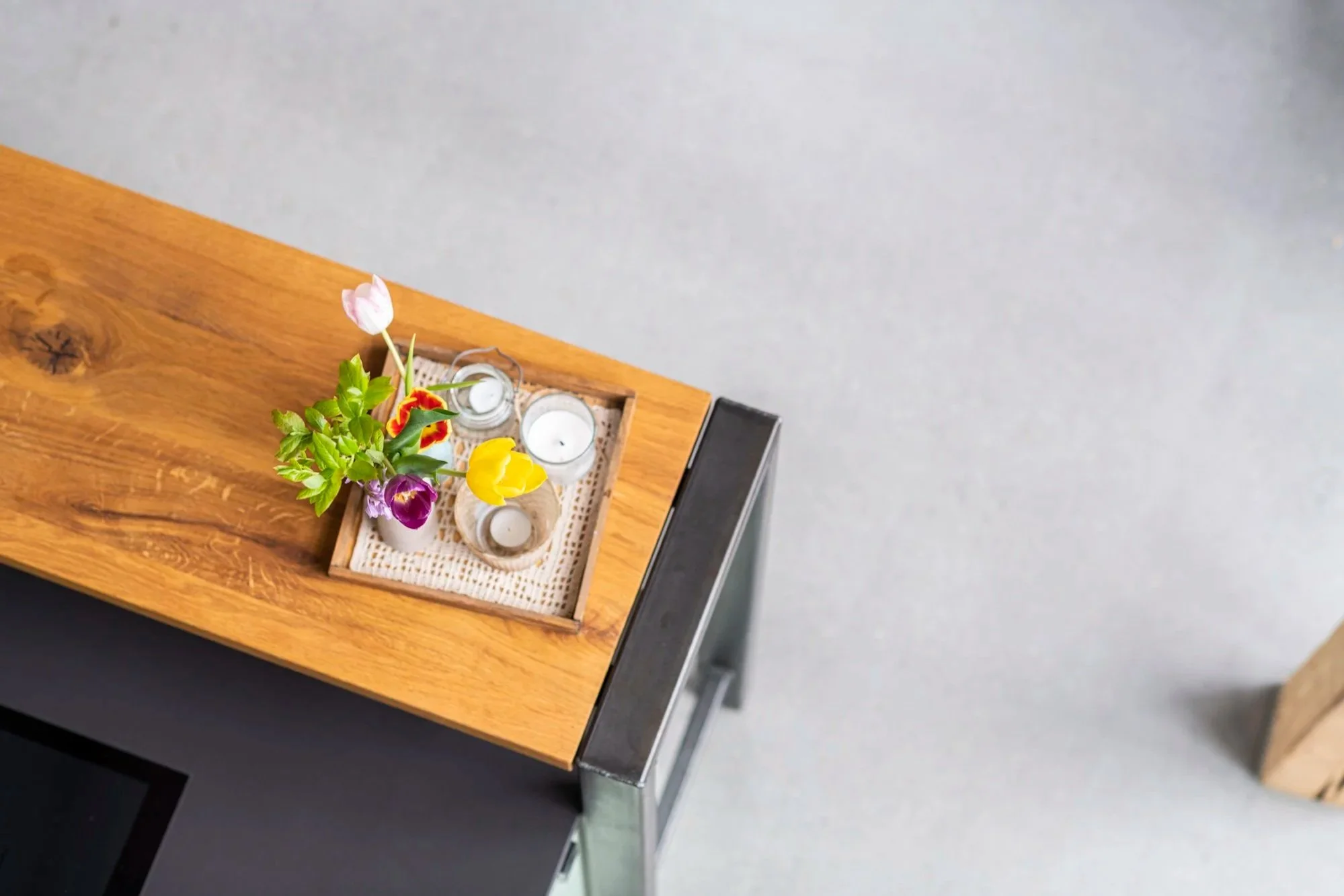 Blumen in einer Holschale mit Kerzen auf einem Holztisch, Blick von oben.