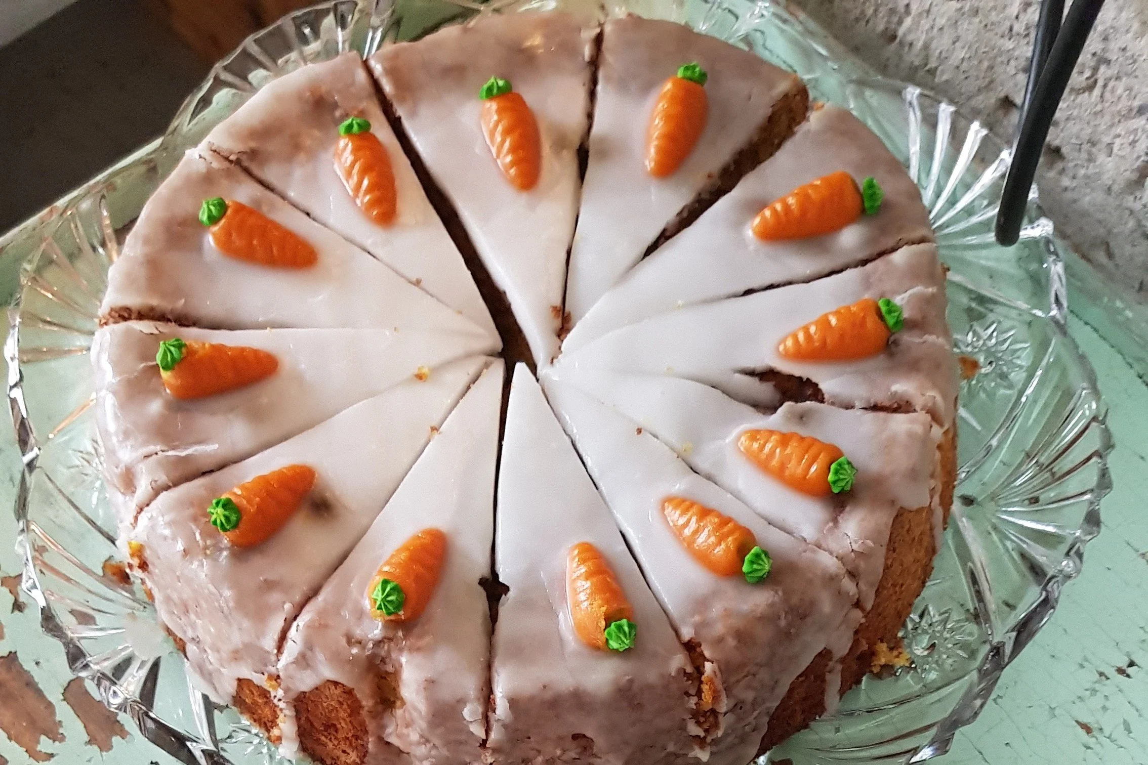Ein Kuchen, dekoriert mit kleinen Marzipan-Karotten auf weißer Glasur, auf einem Kristallglas-Teller