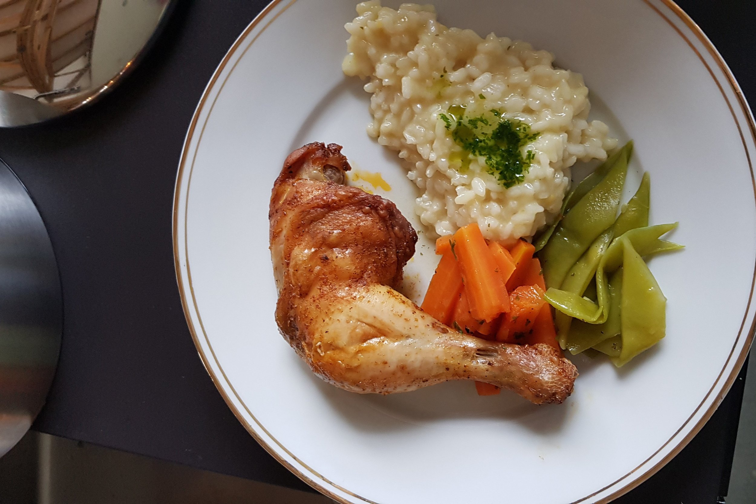 Ein Teller mit gebratenem Hühnchen, Kartoffelbrei mit Kräutern, Karotten und grünen Bohnen.