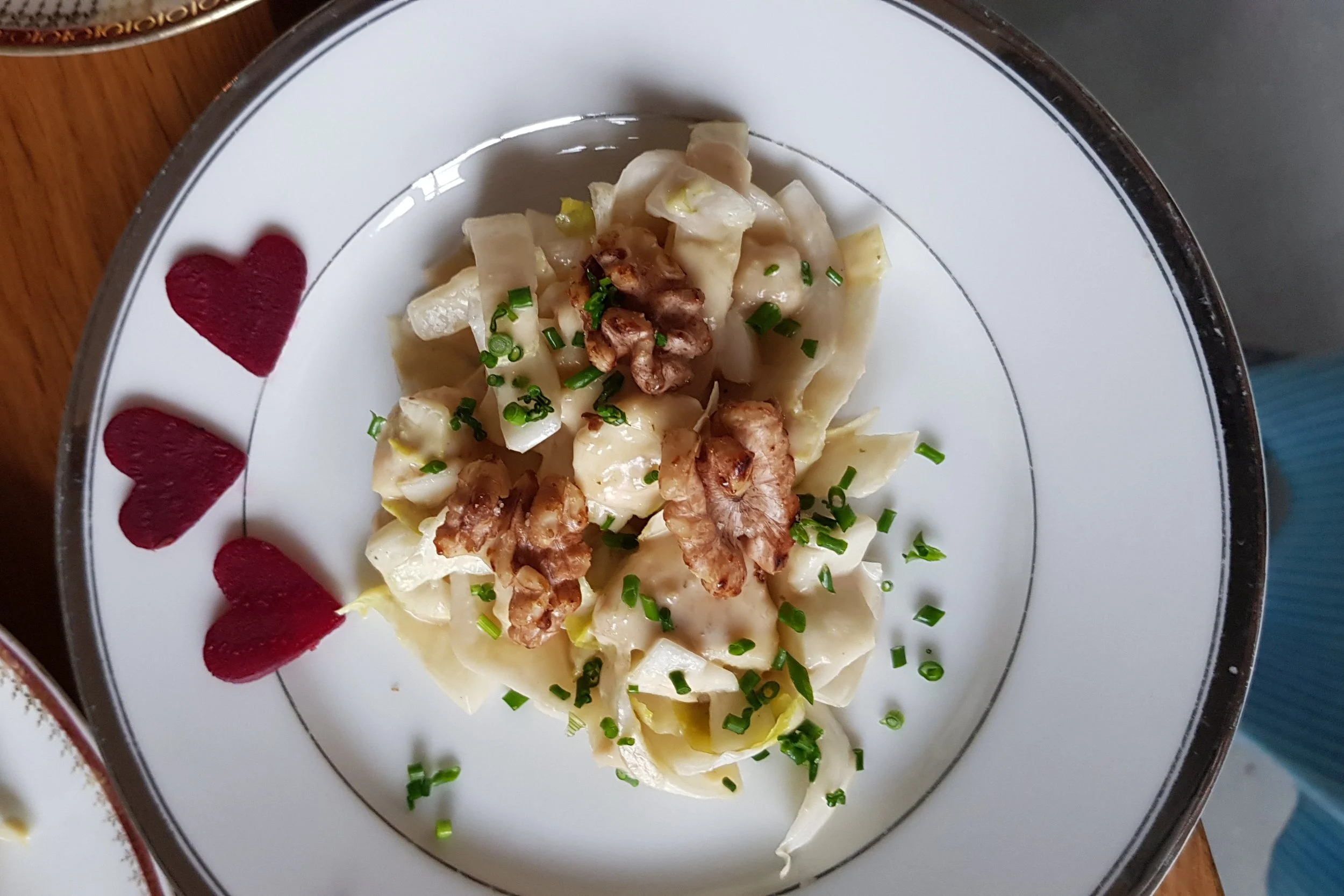 Nudeln mit Walnüssen und Schnittlauch auf einem weißen Teller mit rotem Herzmuster.