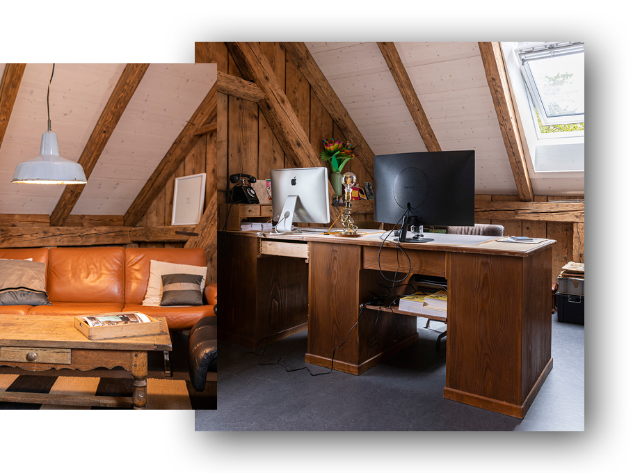 Ein Wohnzimmer und ein Büro in einem Dachgeschoss mit Holzwänden und -decken, ein Ledersofa und ein Holztisch im Wohnzimmer, ein Arbeitsplatz mit Computer, Monitor und Büromaterialien im Büro, beide Räume sind gut beleuchtet durch ein Dachfenster.