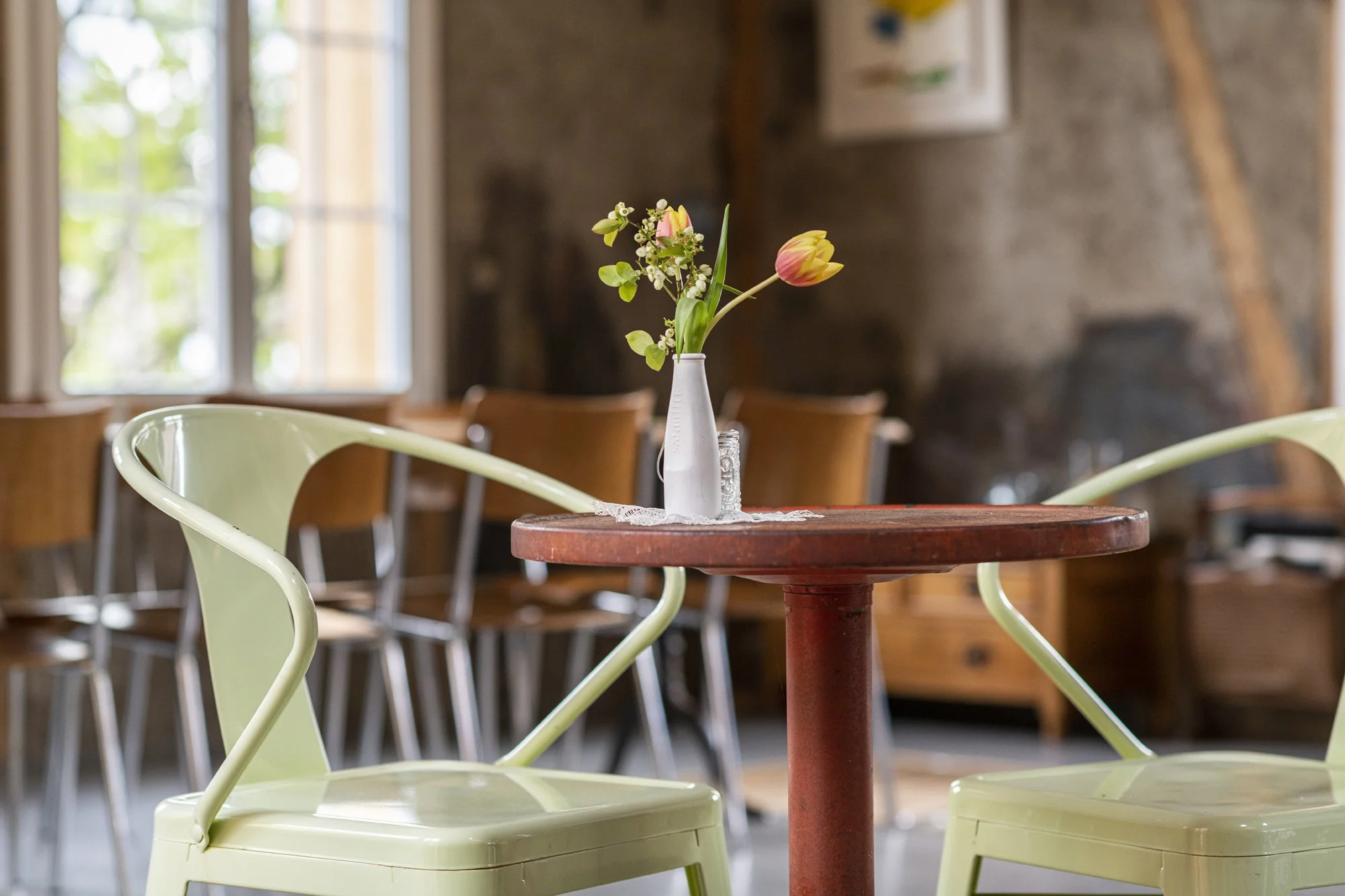 Ein roter Tisch mit einer Vase mit Tulpen und kleinen Blumen in der Alten Wagnerei mit Holzwänden und mehreren Stühlen.