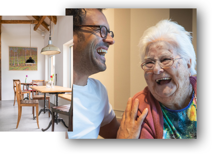 Ein Mann und eine alte Frau lachen und scheinen sich zu unterhalten in einem freundlichen Innenraum, mit herzlichem Händchenhalten.