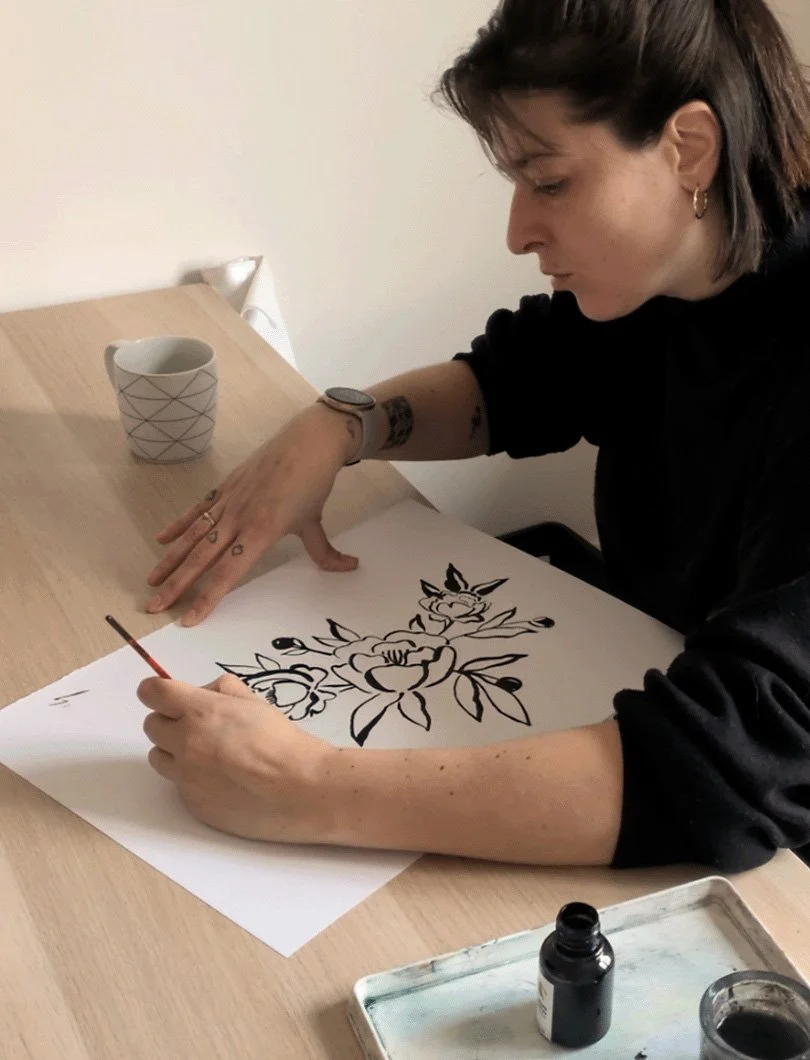 Portrait de Noa Serica en train de peindre à l'encre de Chine pour un tatouage floral