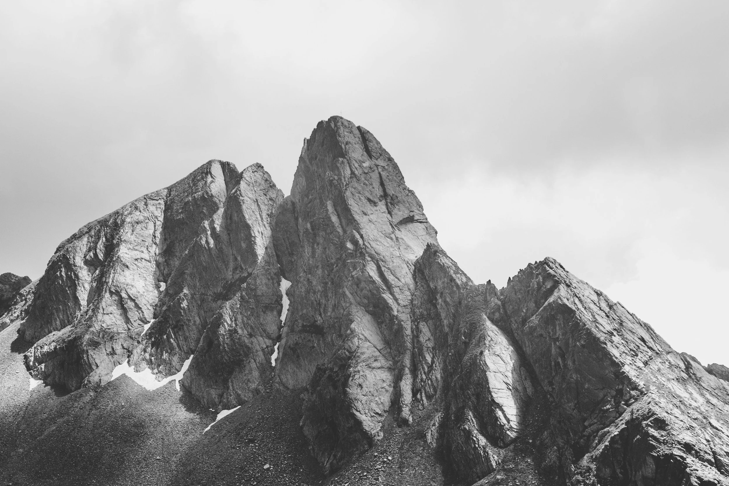 Black and white photograph of rugged mountain peaks with sharp, jagged rocks and steep slopes.