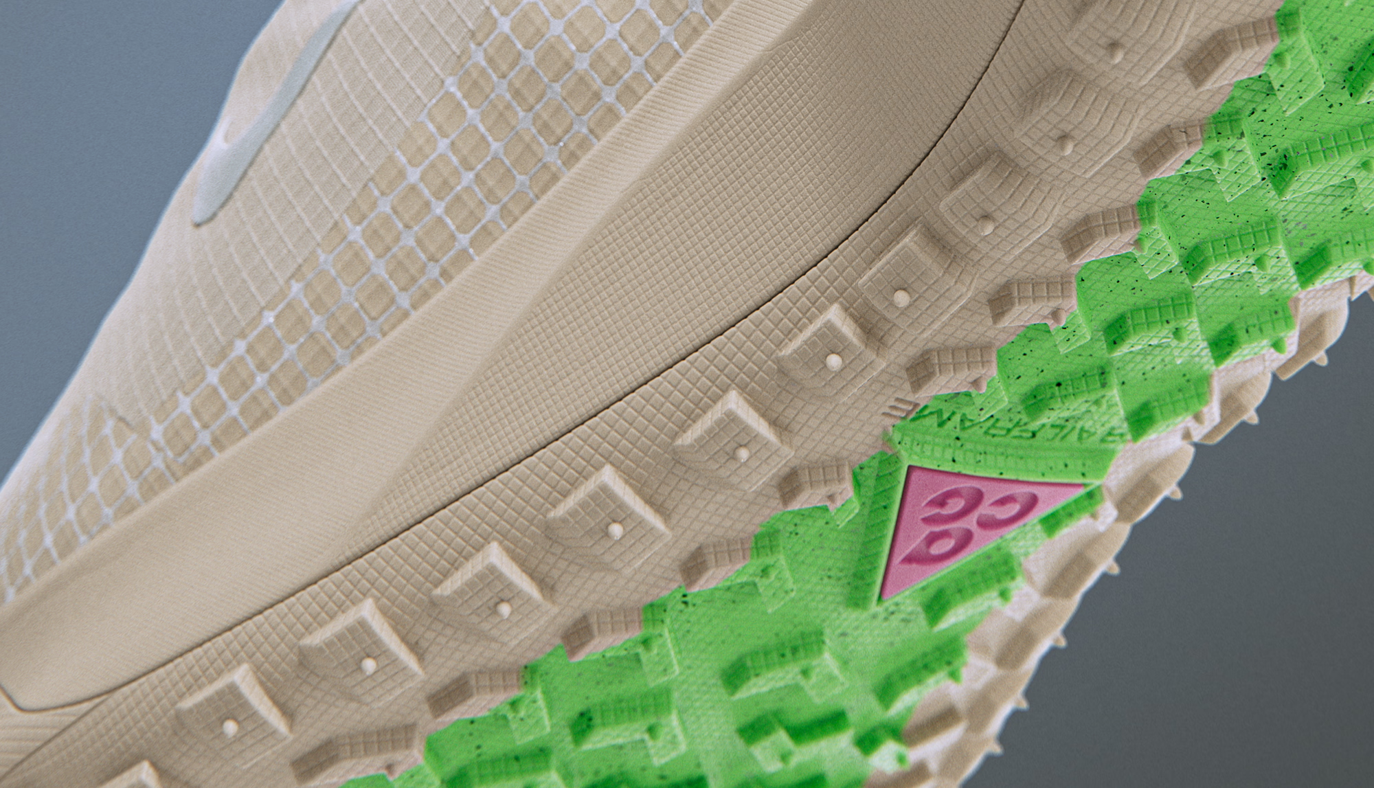 Close-up of the sole of a beige athletic shoe with green and pink accents, showing textured patterns and tread design.