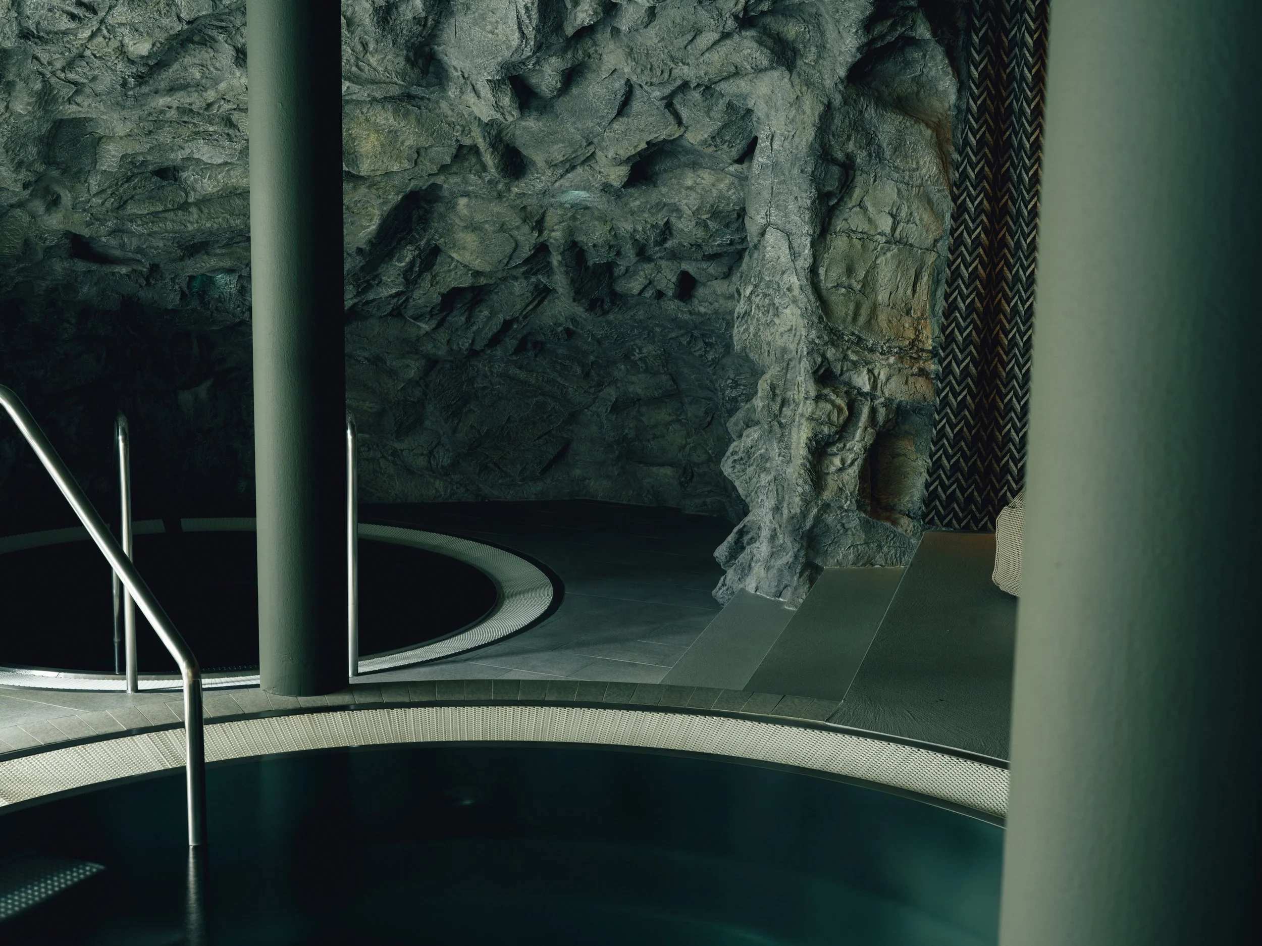Indoor pool area with a rock wall, metal handrails on the pool stairs, and patterned curtain on the right side.