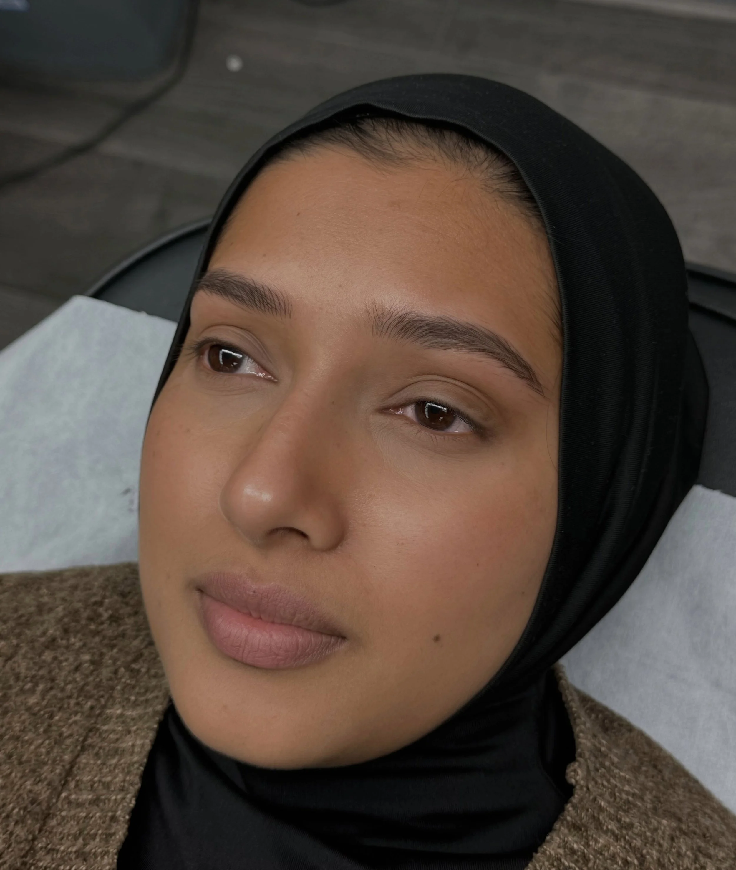 Close-up of a person's face lying on the ground, wearing a black hoodie, with a calm expression and detailed skin and eye features.