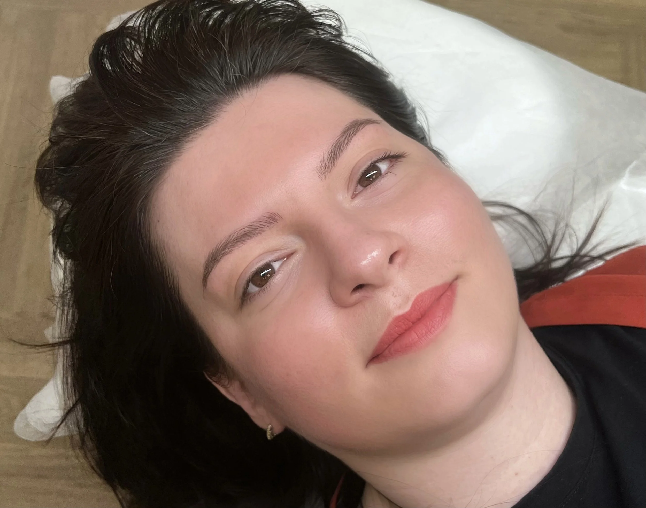 Close-up of a woman lying on a white surface, possibly a medical or beauty clinic table, with dark brown hair and bright skin.