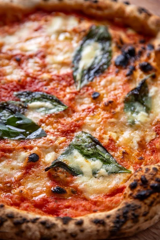 Close-up of a Margherita pizza with melted cheese, fresh basil leaves, and a crispy crust.
