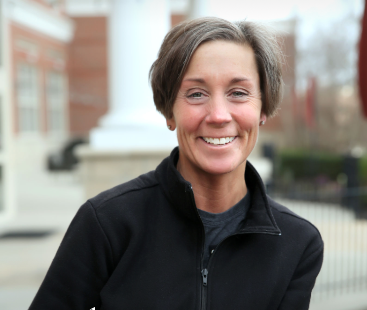 A woman with short brown hair smiling outdoors in front of a brick building with white columns.