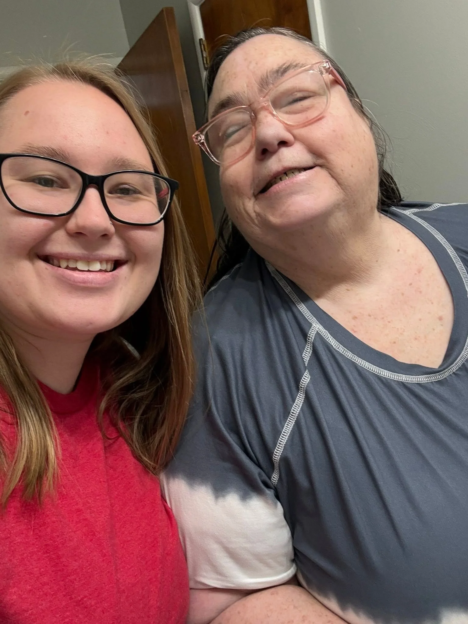 A young woman with long brown hair and glasses smiling next to an older woman with glasses, gray hair, and freckles, who is also smiling.