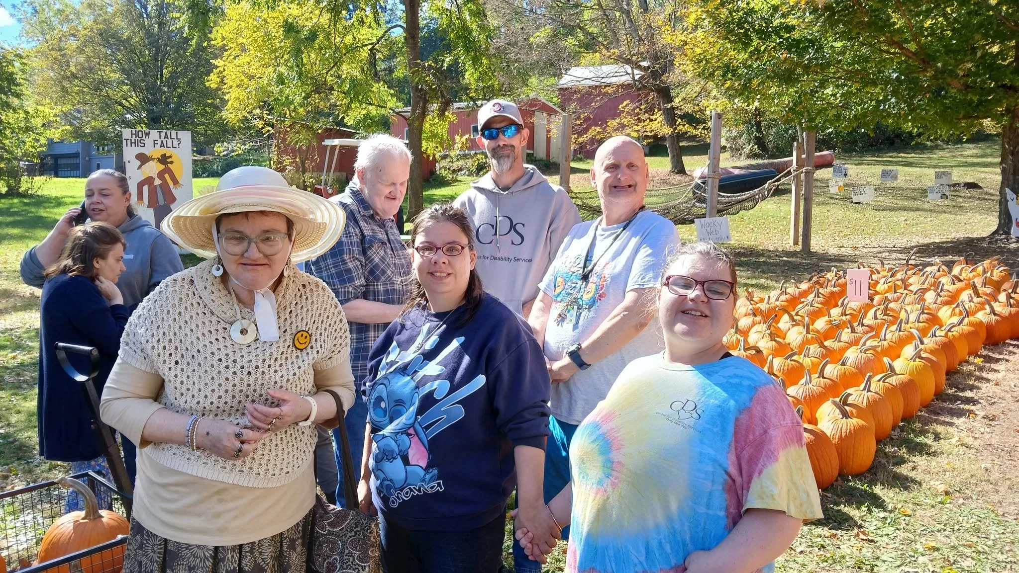 A group of people at a pumpkin patch, with pumpkins arranged on the ground and trees in the background during daytime.