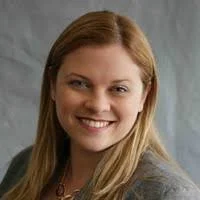 A woman with long blonde hair smiling at the camera against a neutral background.