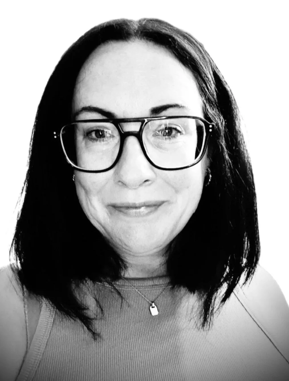 Black and white photo of a woman with shoulder-length dark hair, glasses, and a subtle smile, wearing a sleeveless top and a necklace with a pendant.