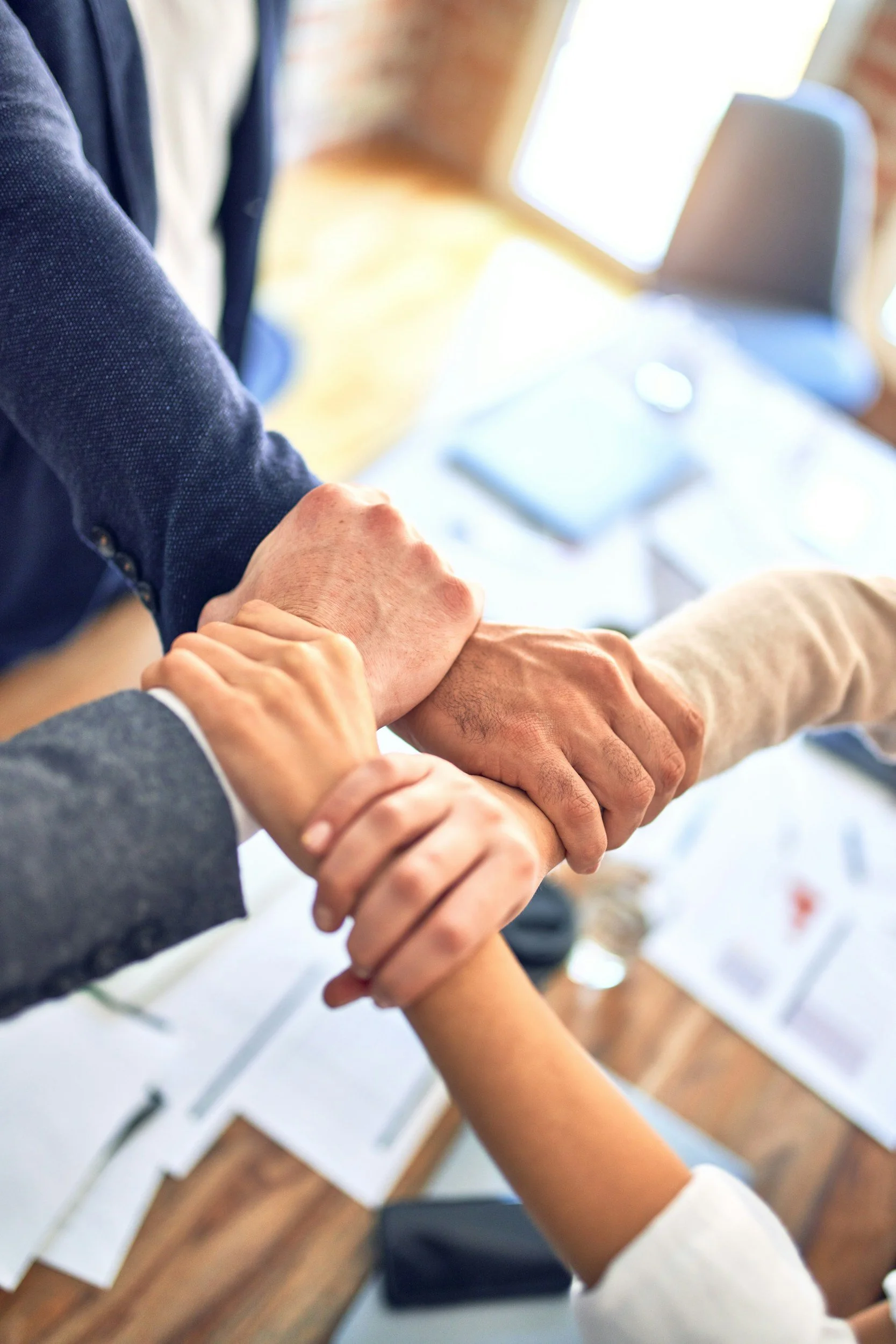 Several people holding hands in a circle, showing unity or teamwork, in an indoor setting with bright natural light.