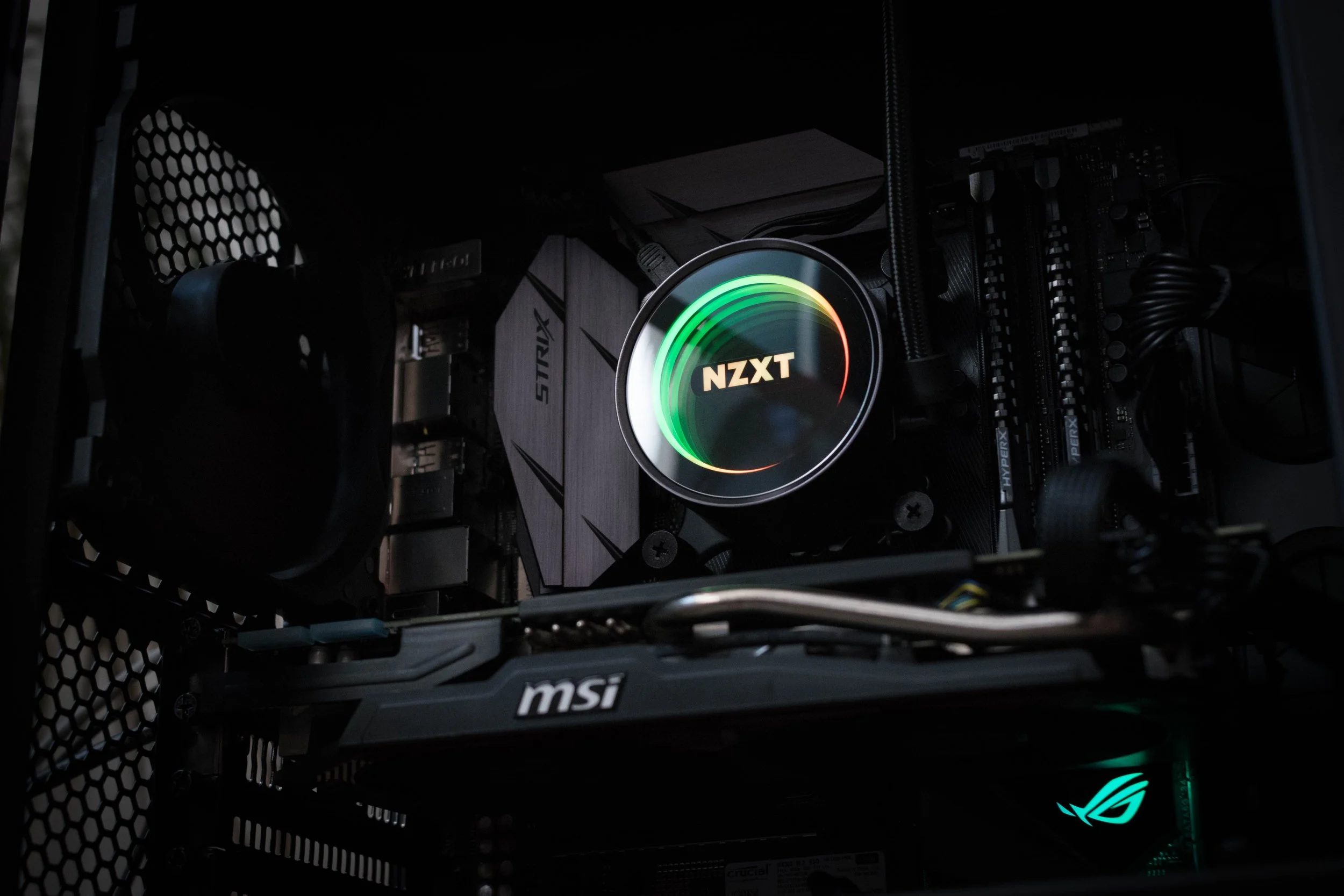 Inside a computer case, a graphics card branded MSI, a Cooler Master power supply, an NZXT liquid cooling pump with a glowing NZXT logo, and other components are visible.