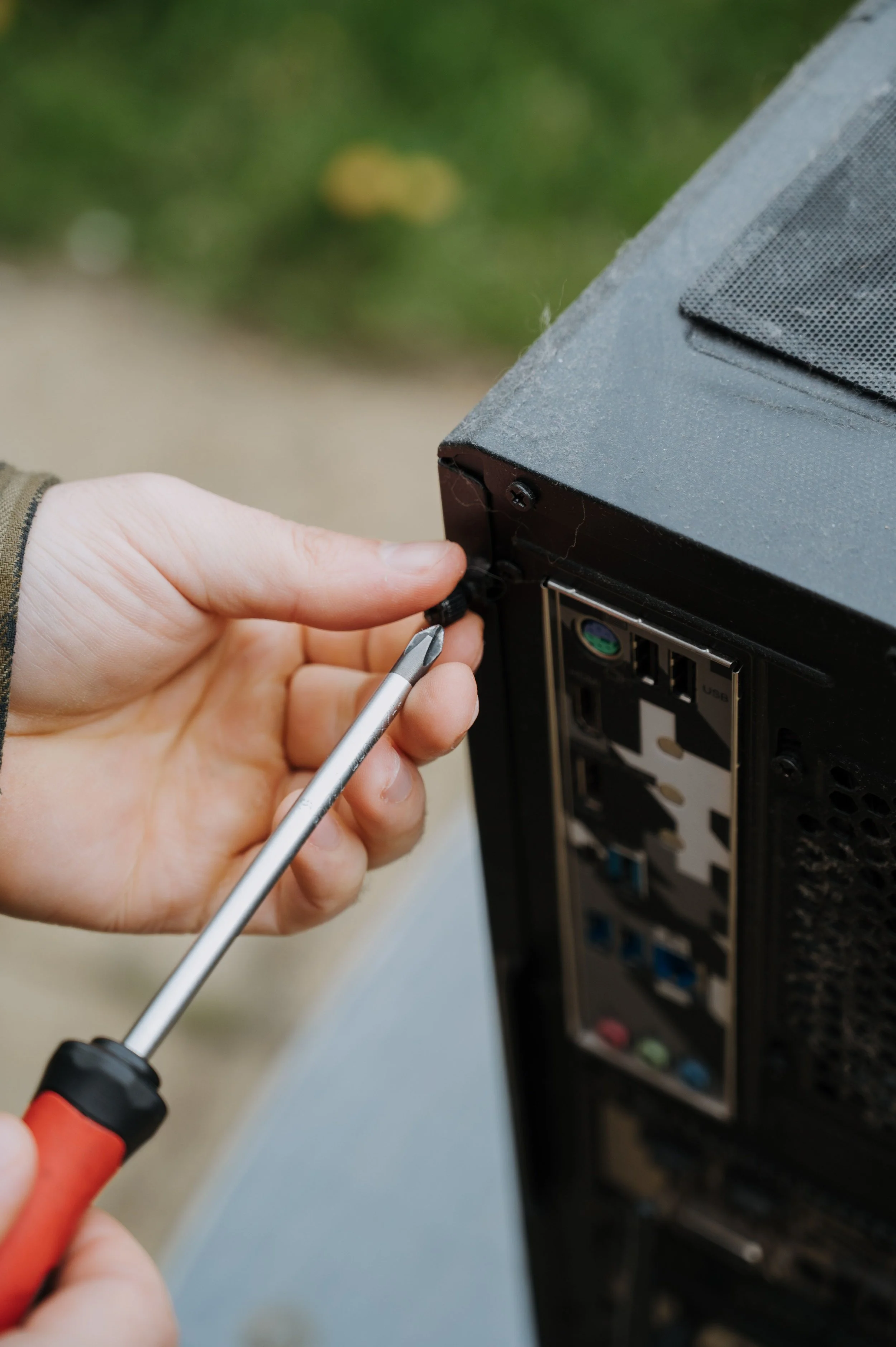 Close-up of a person using a screwdriver to remove a screw from a computer tower's back panel.