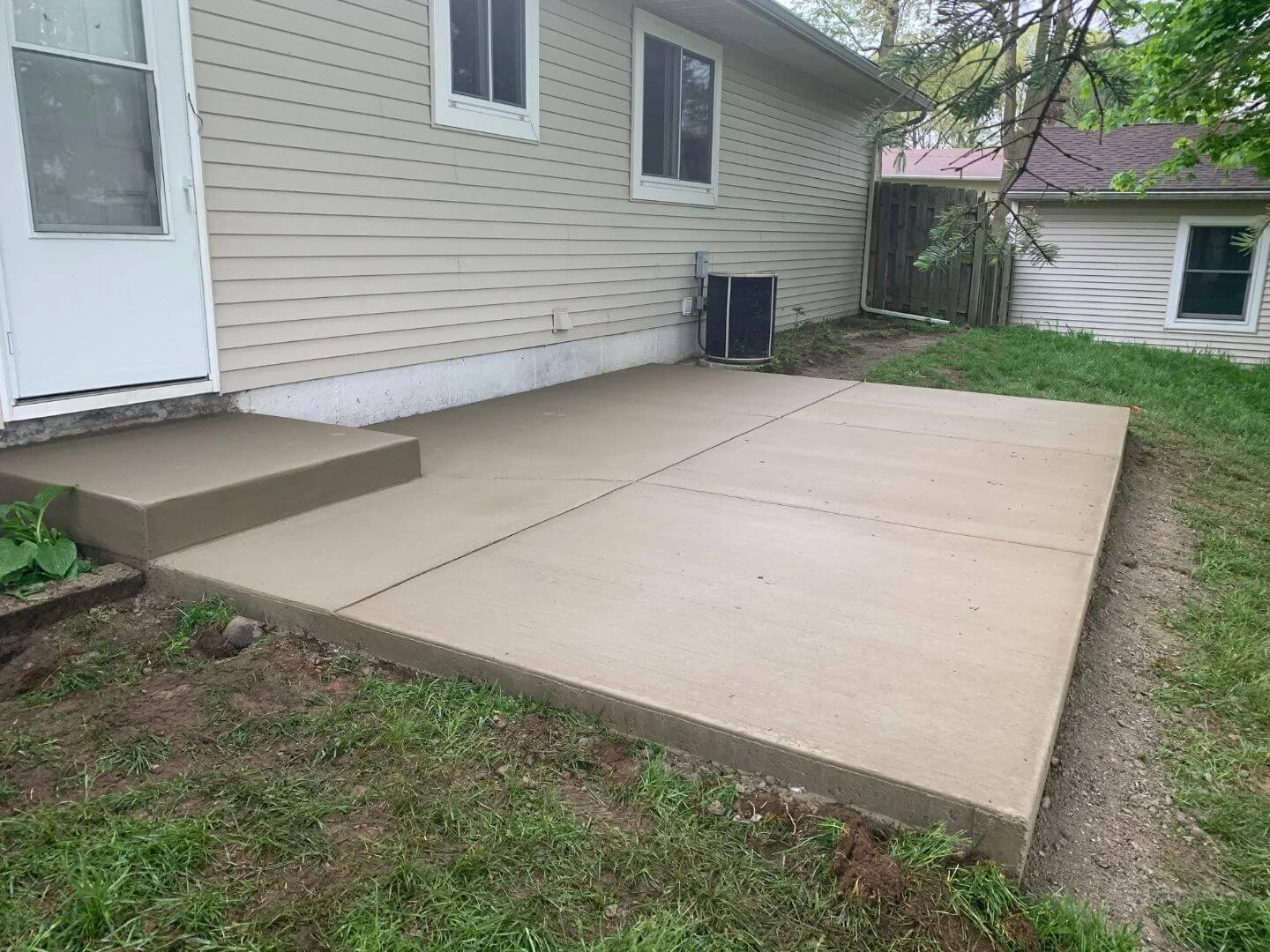 Finished concrete patio with steps outside a house, with grass and dirt surrounding it.