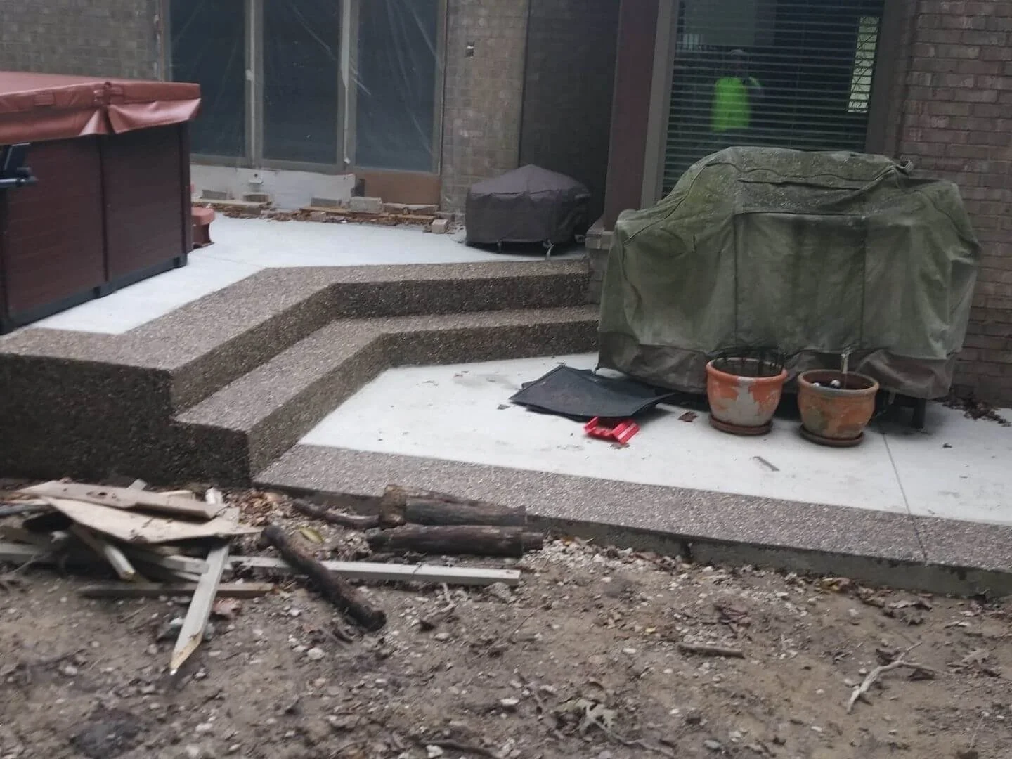 Backyard patio with stone steps and potted plants, covered grill, nearby mailbox, and construction debris in the foreground.